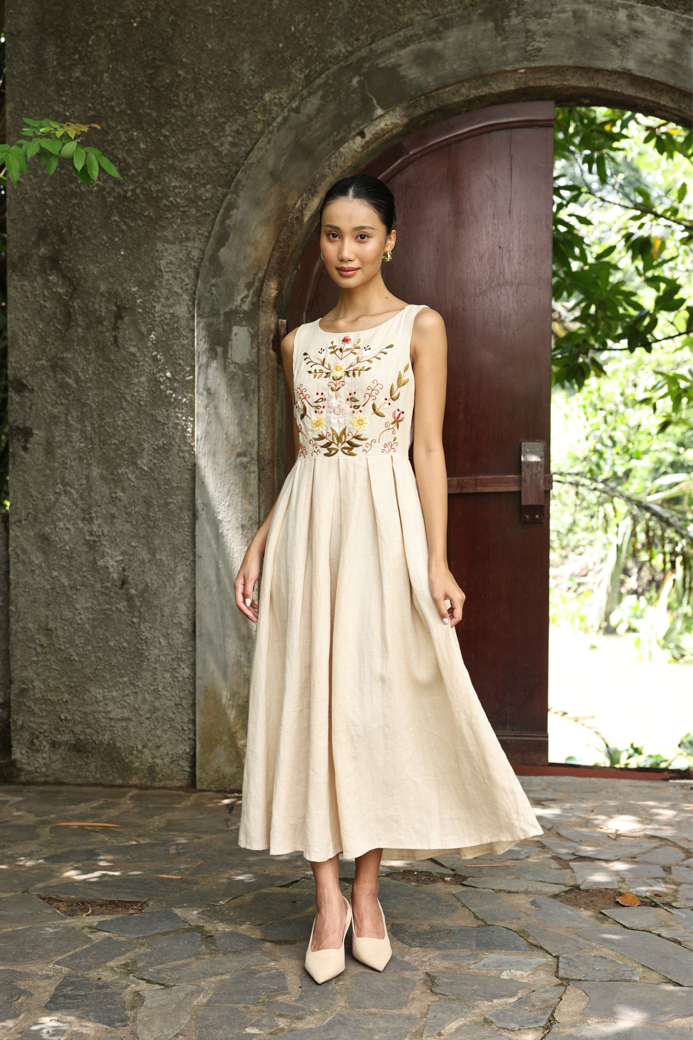 Woman in a floral dress standing in front of a stone archway with greenery.