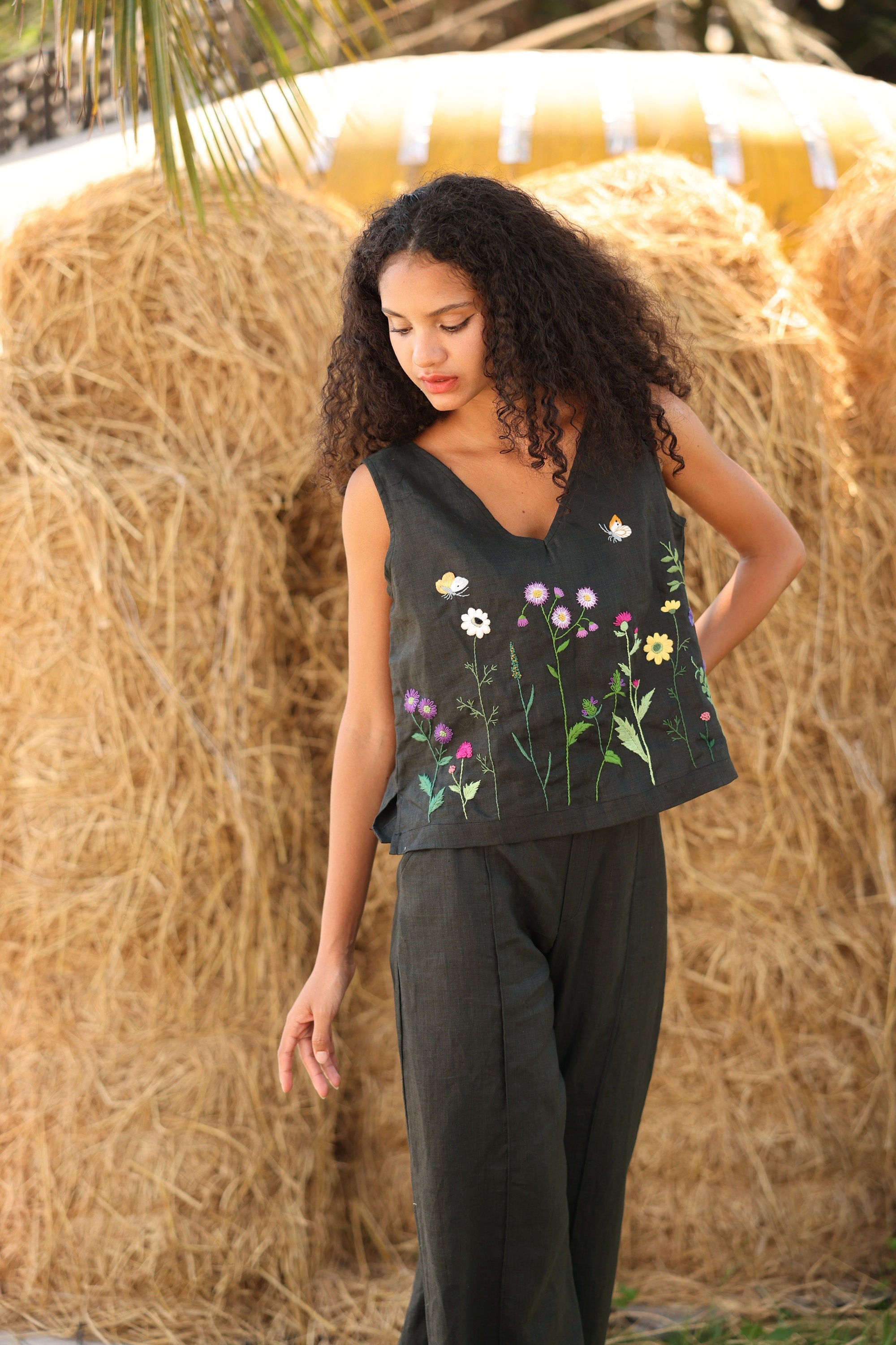 Woman wearing a sleeveless top with floral designs in front of hay bales.