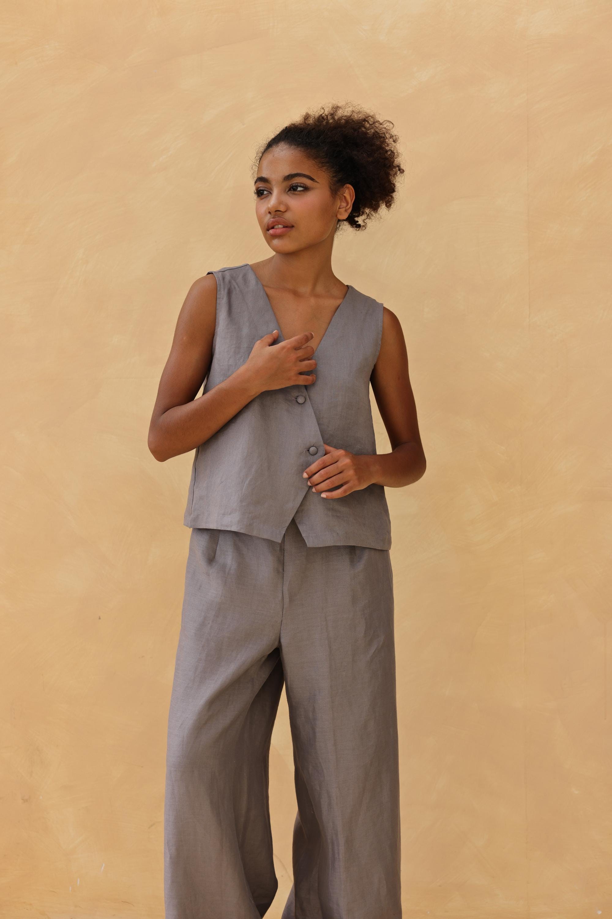 Woman wearing a gray sleeveless top and pants against a beige background