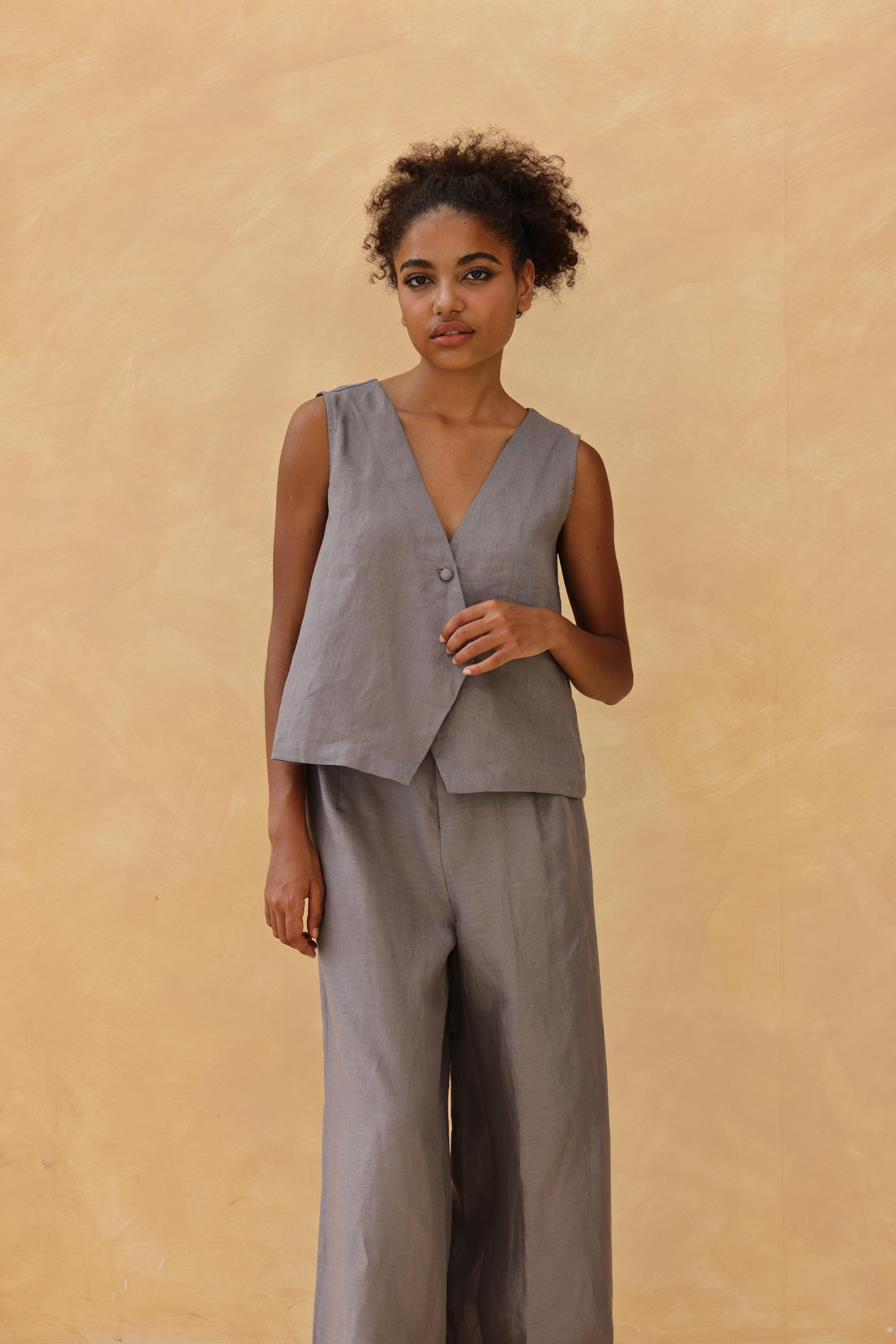 Woman wearing a gray sleeveless top and pants against a beige background