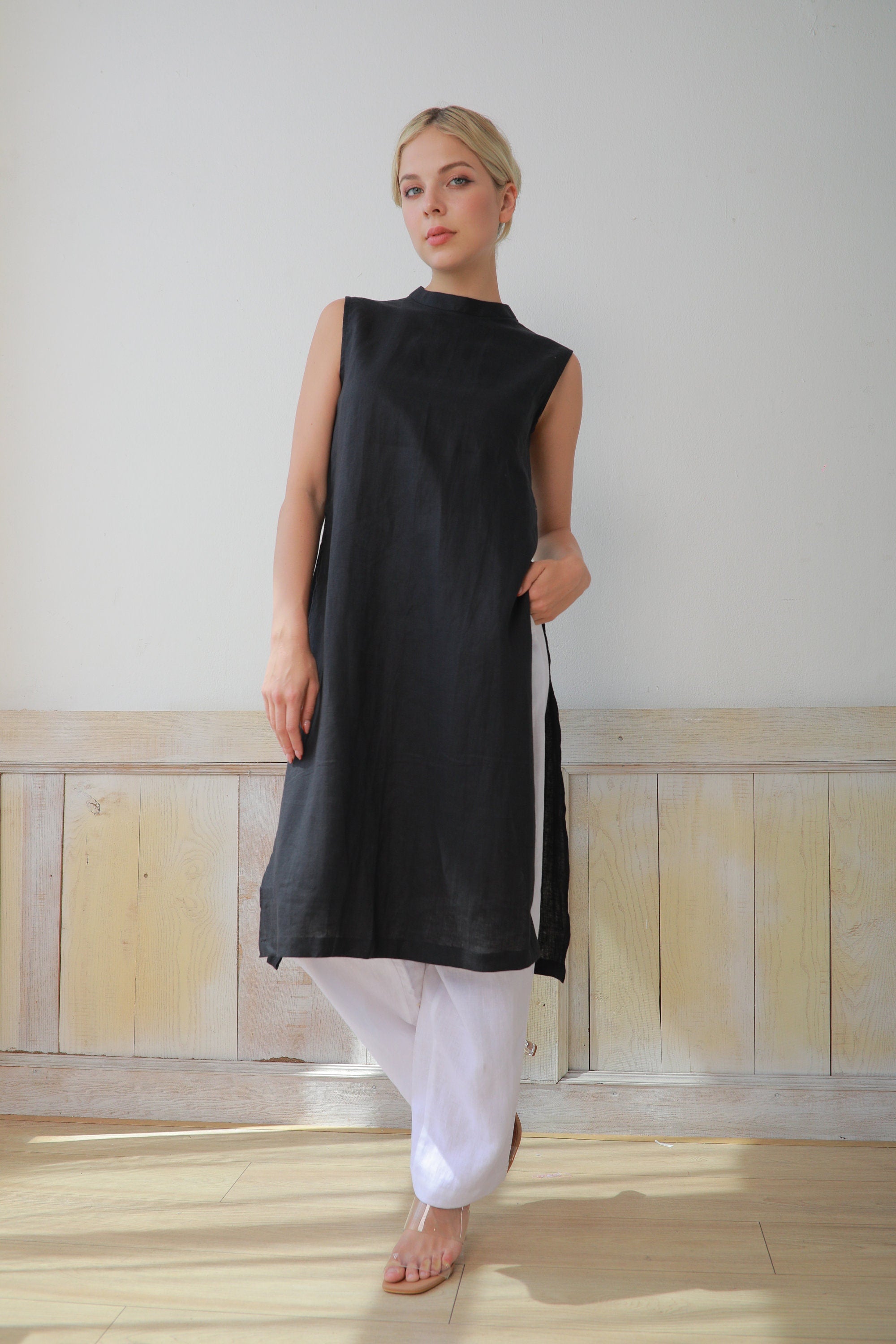 Woman wearing a black sleeveless top and white pants against a plain background