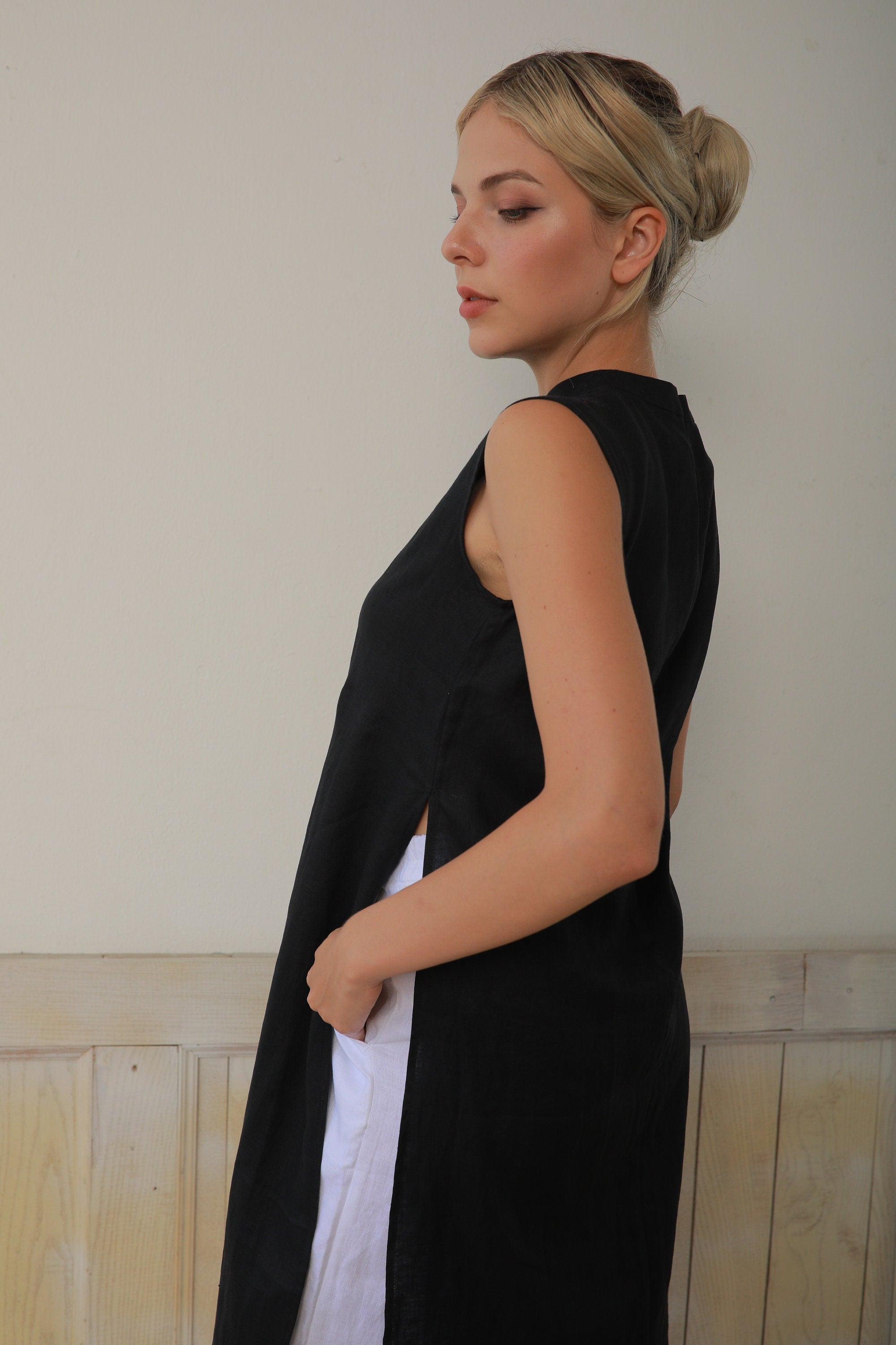 Woman wearing a black sleeveless dress against a light-colored wall.