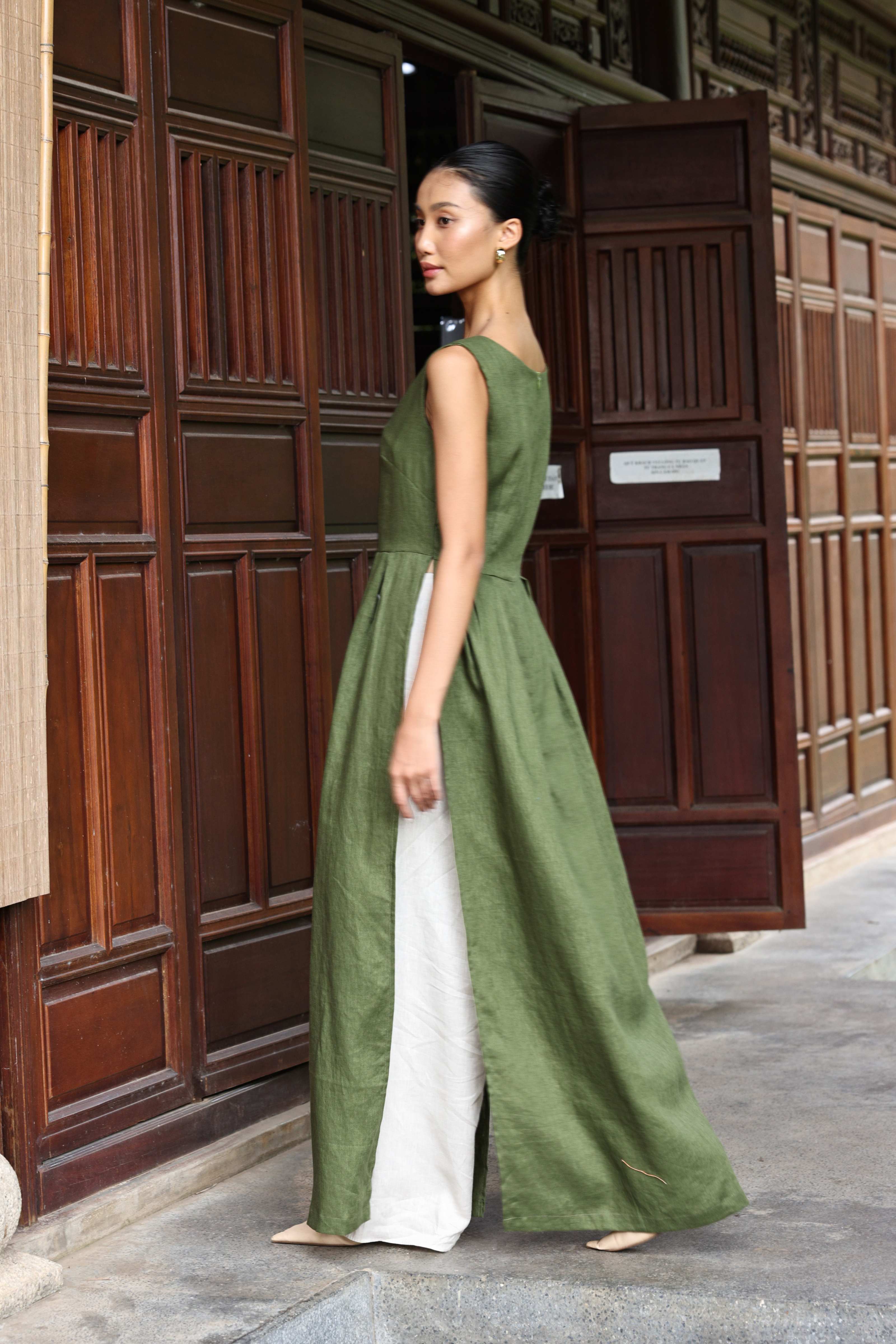 Woman wearing a green tunic and white pants standing in front of wooden panels.