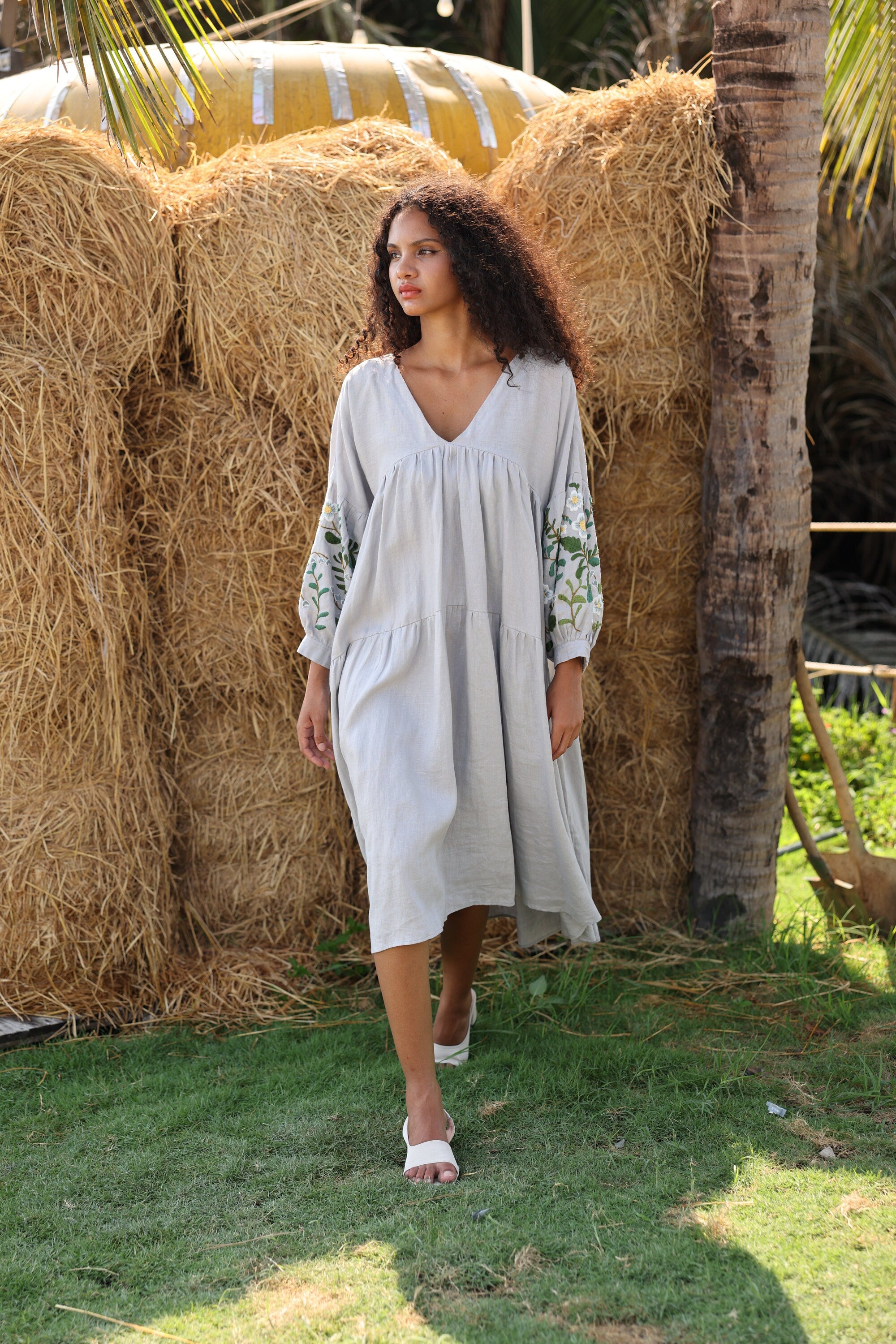Woman in a dress standing in front of hay bales with palm trees in the background