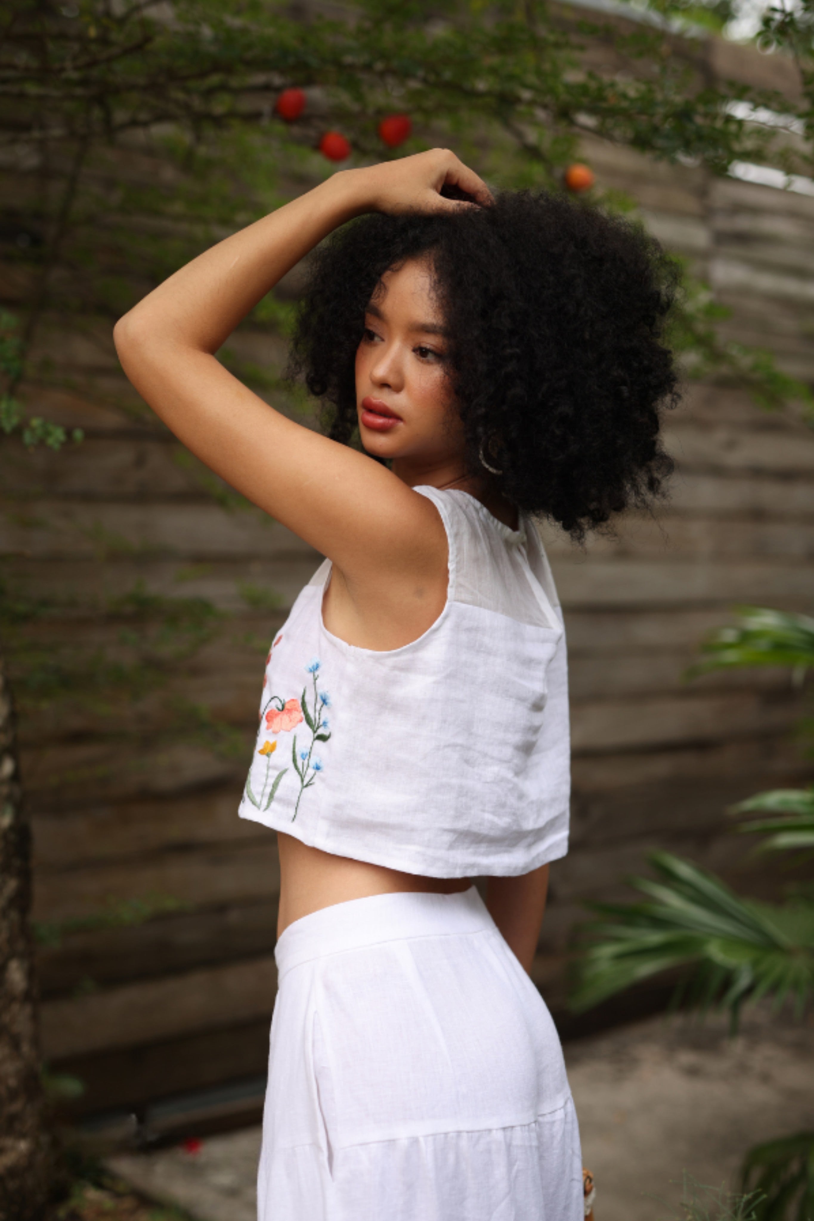 Woman in a white outfit with floral design standing outdoors with greenery in the background