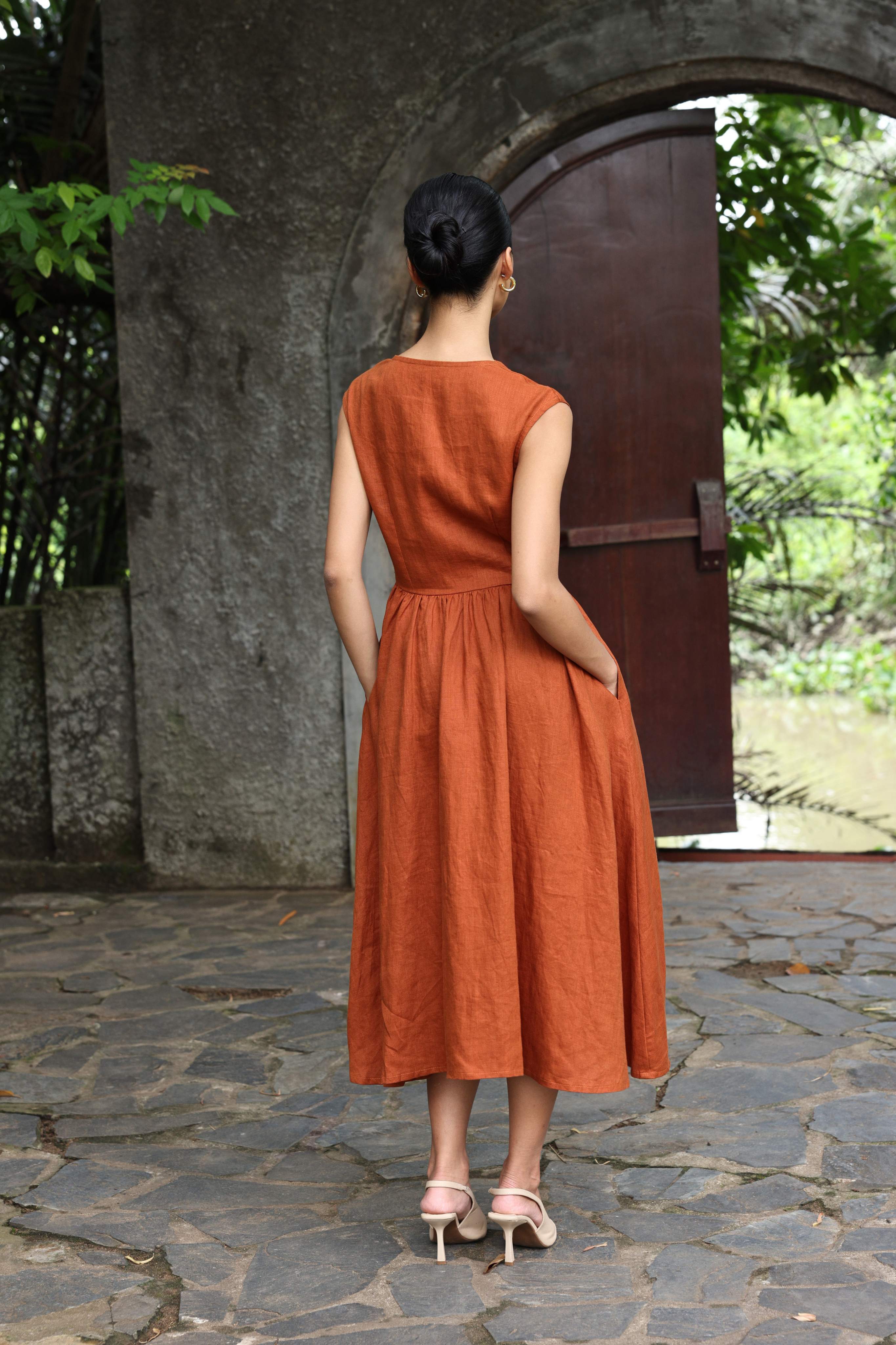 Woman in an orange dress standing in front of a stone archway with greenery.