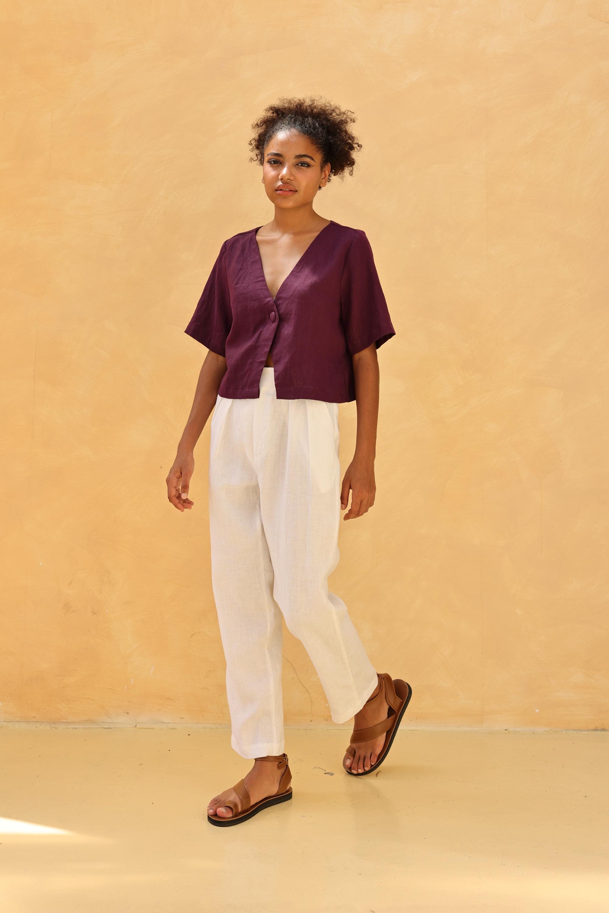 Woman wearing a top and white pants against a beige background