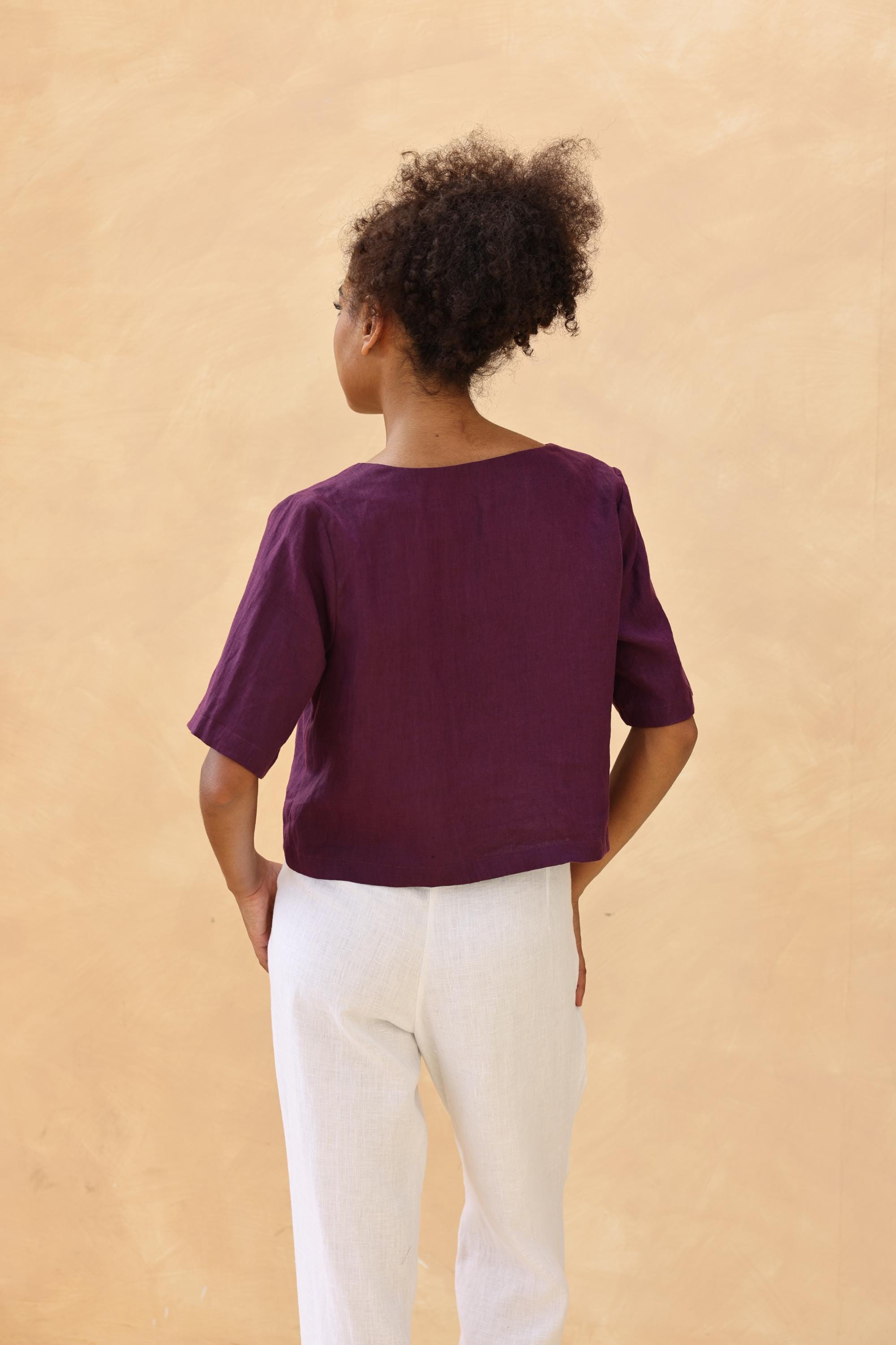 Person wearing a purple top and white pants against a beige background