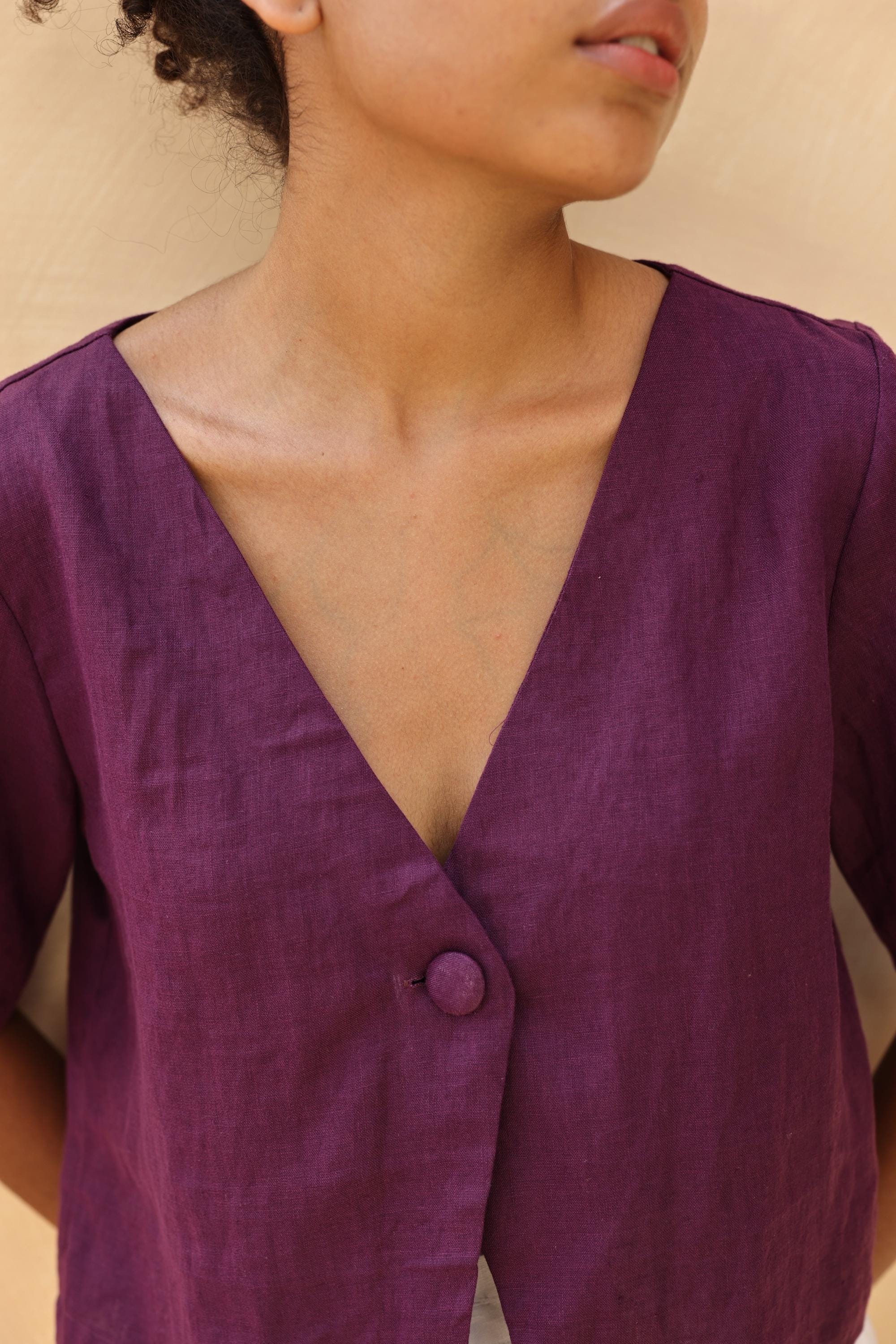 Close-up of a person wearing a purple outfit with a button detail on a beige background