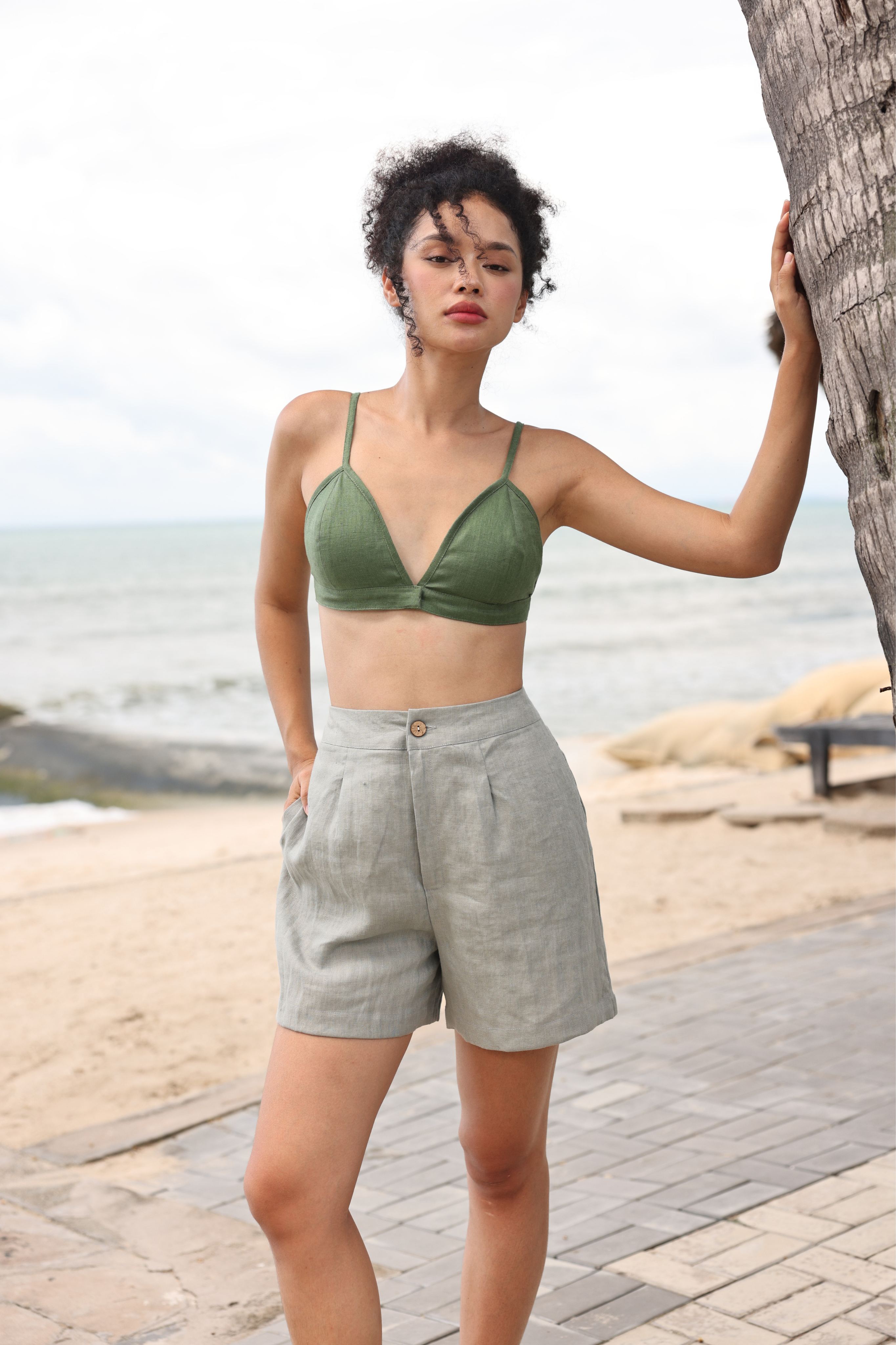Woman in green bikini top and gray shorts standing on a beach path.