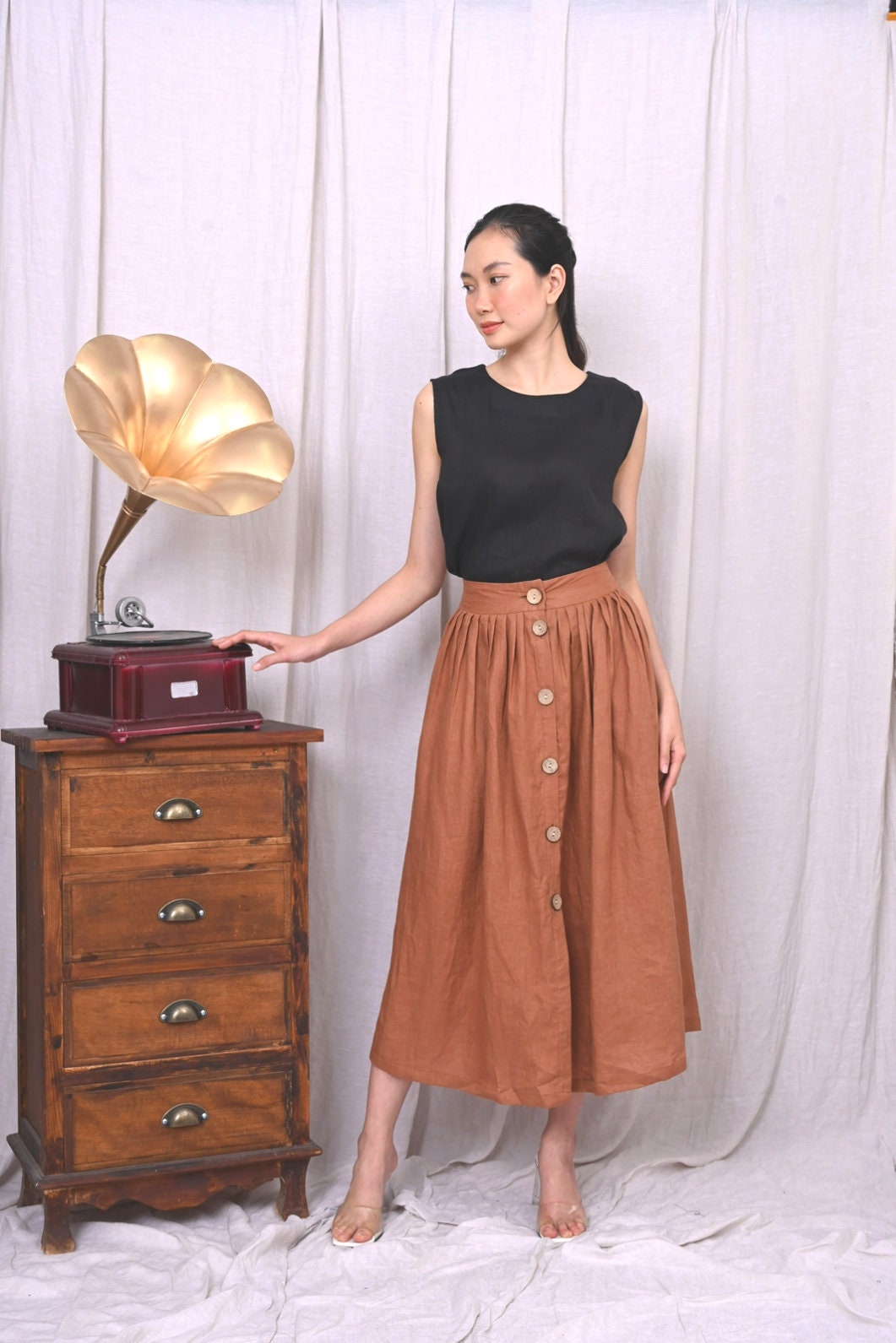Woman in a brown skirt standing next to an old-fashioned gramophone against a white curtain.