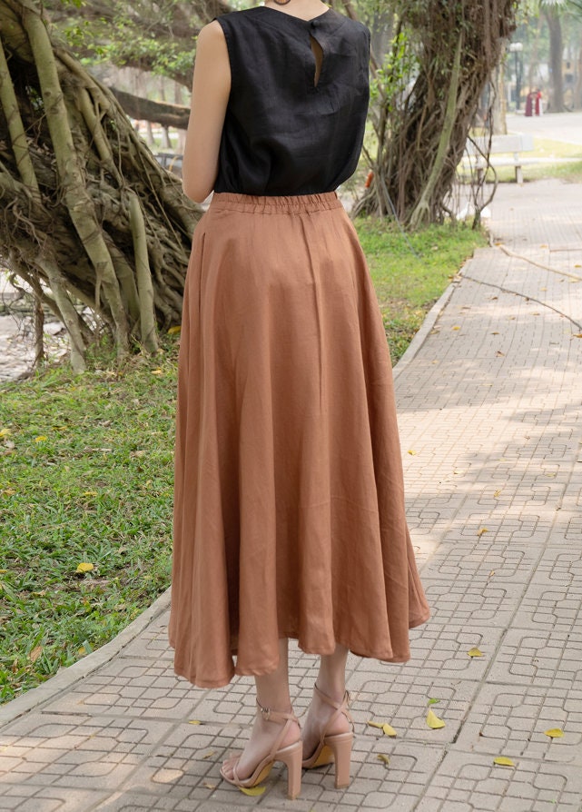 Person wearing a black top and brown skirt walking on a sidewalk with trees in the background