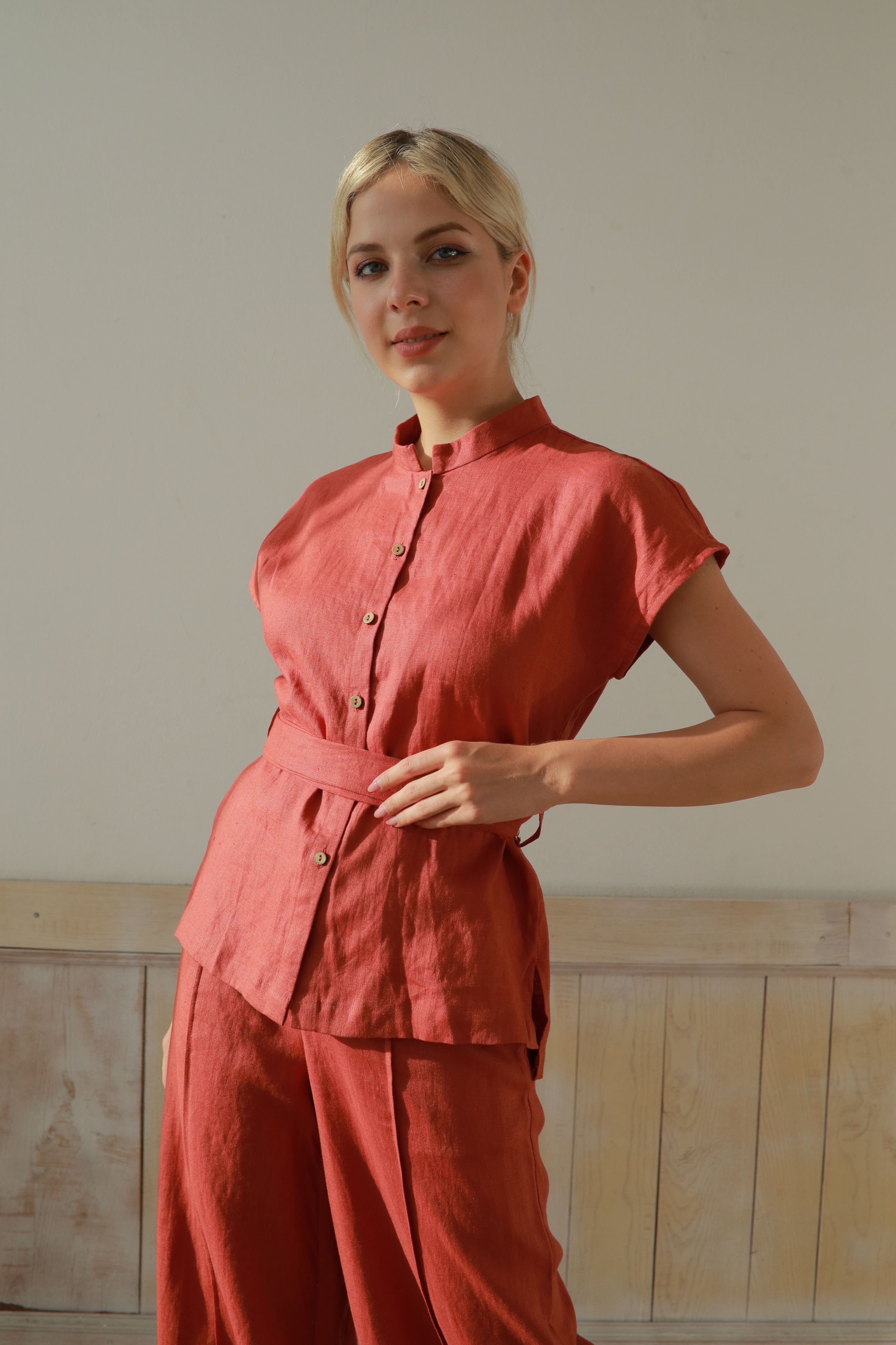 Woman wearing an outfit standing against a plain wall.