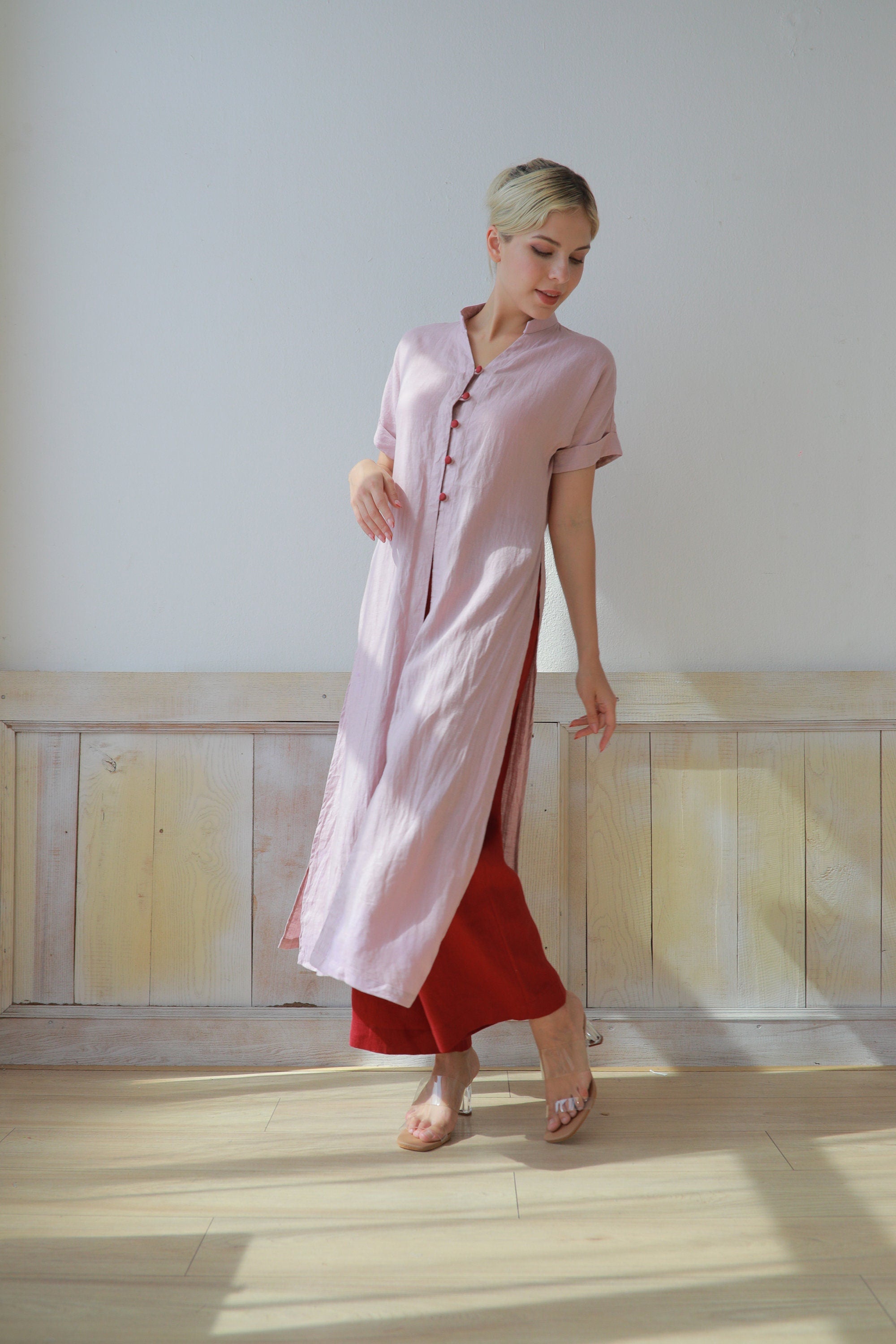 Woman wearing a pink dress with a red skirt against a white wall.