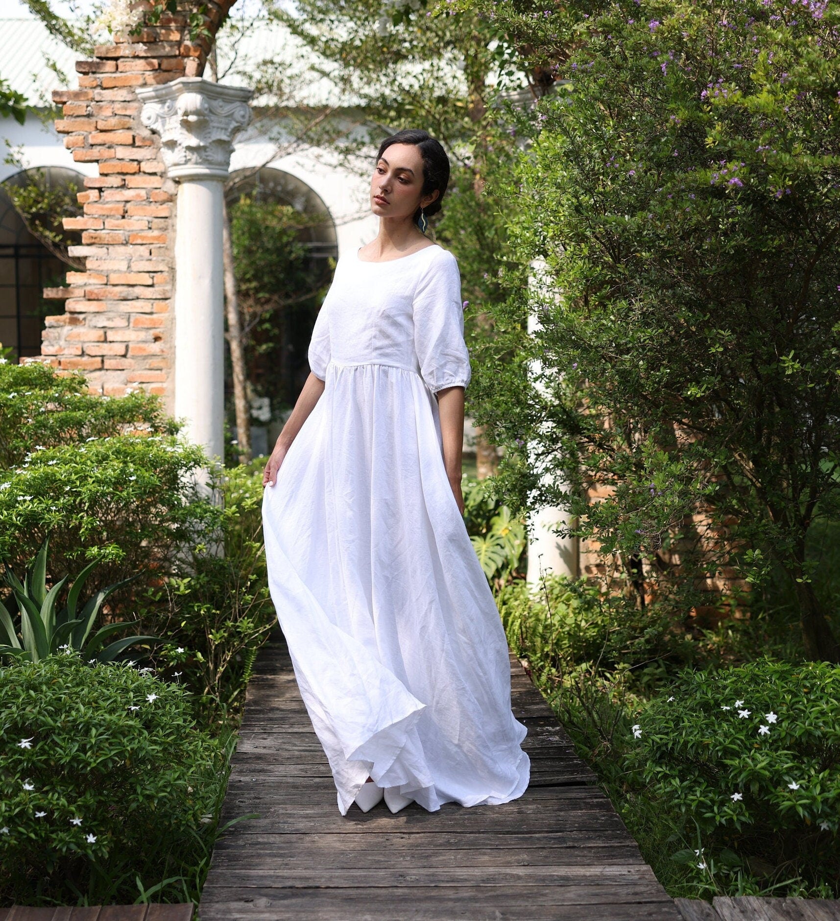 Woman in a white dress standing on a wooden path in a garden setting