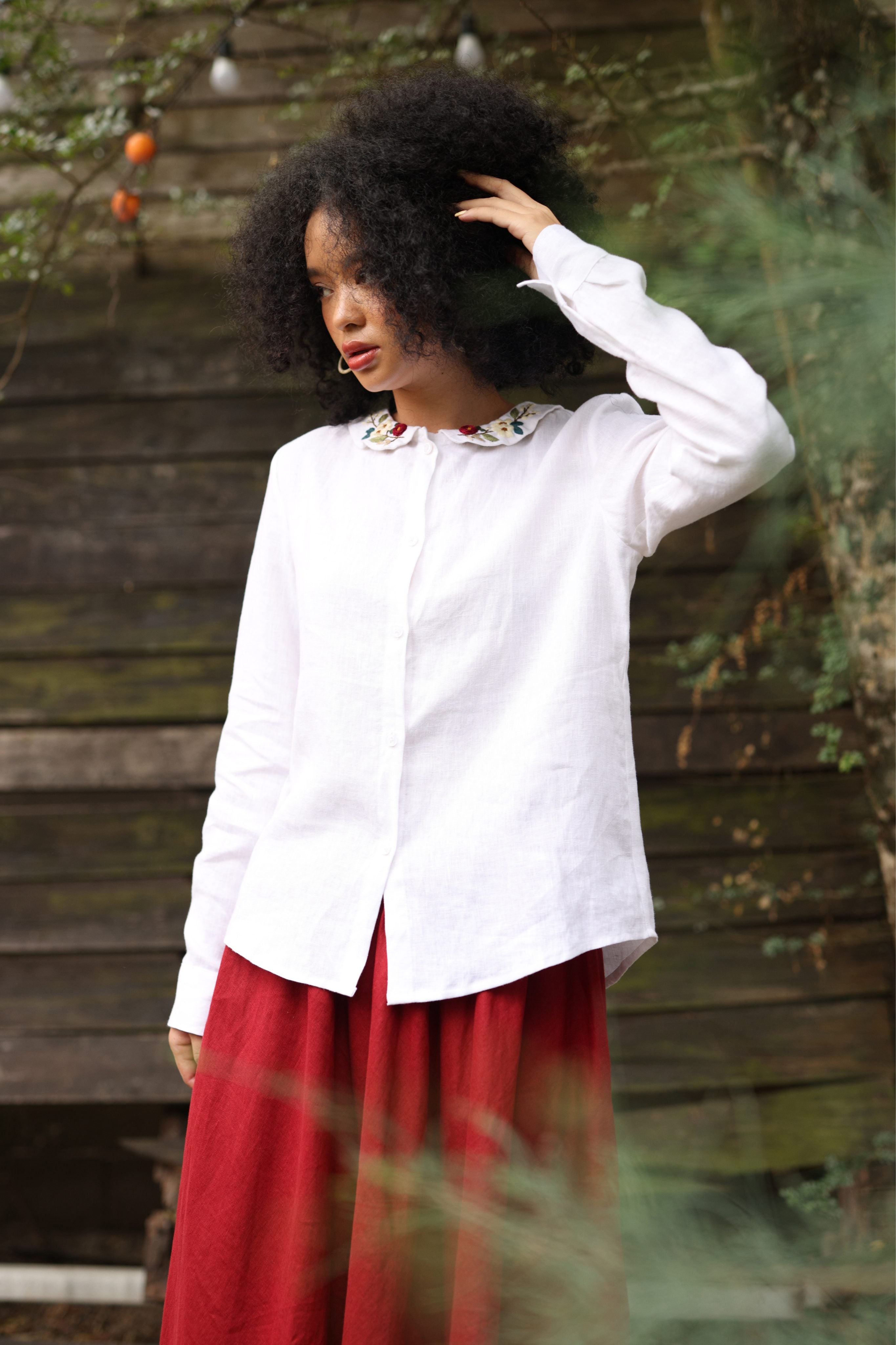 Person wearing a white shirt and red skirt standing against a wooden wall.