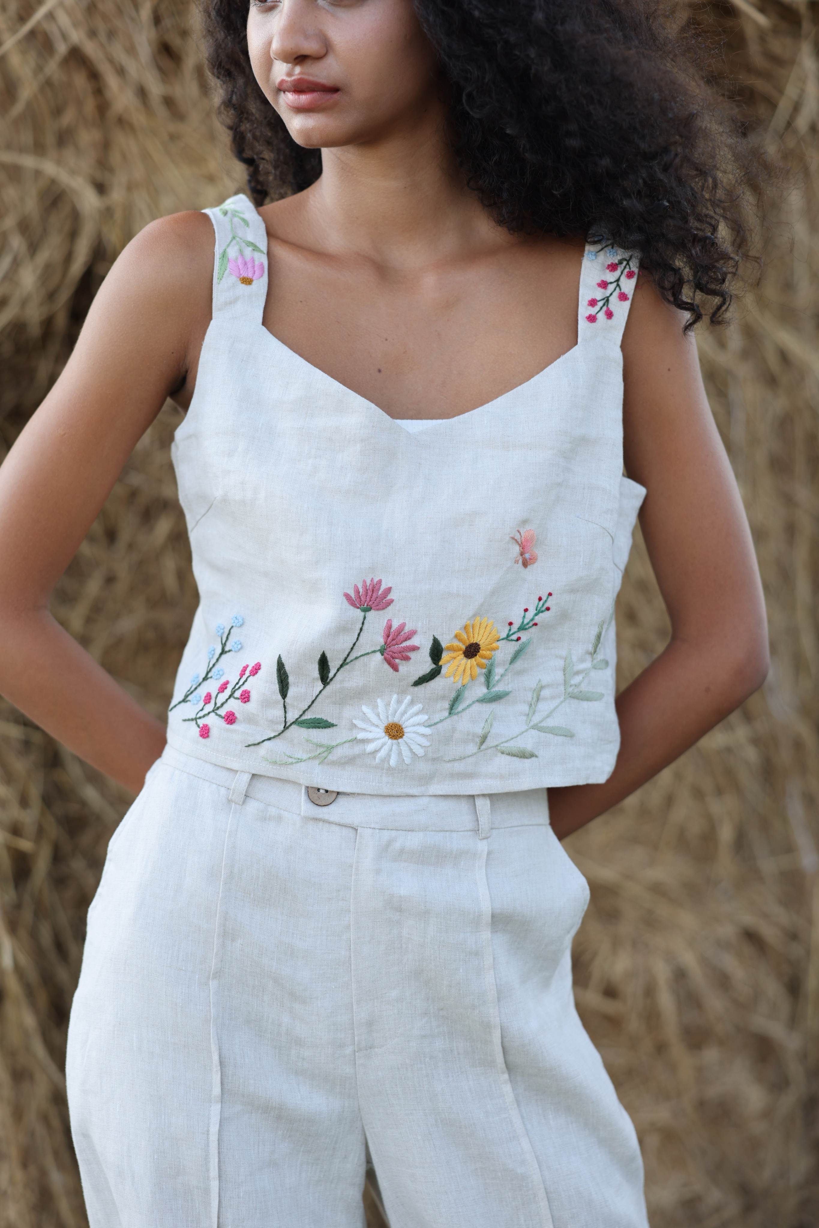 Woman wearing a sleeveless top with floral embroidery against a blurred natural background