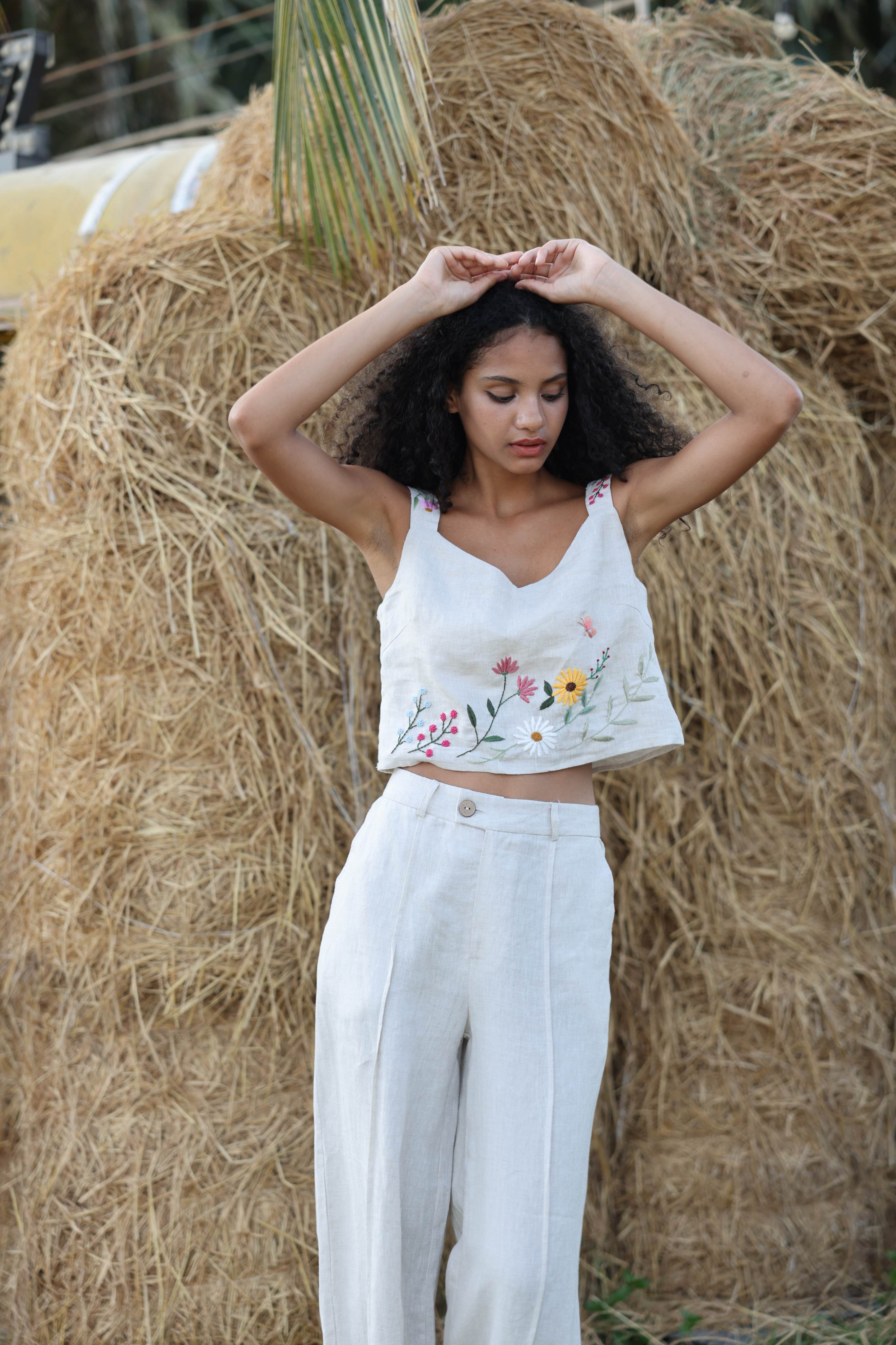 Woman wearing a floral top and pants standing in front of hay bales.