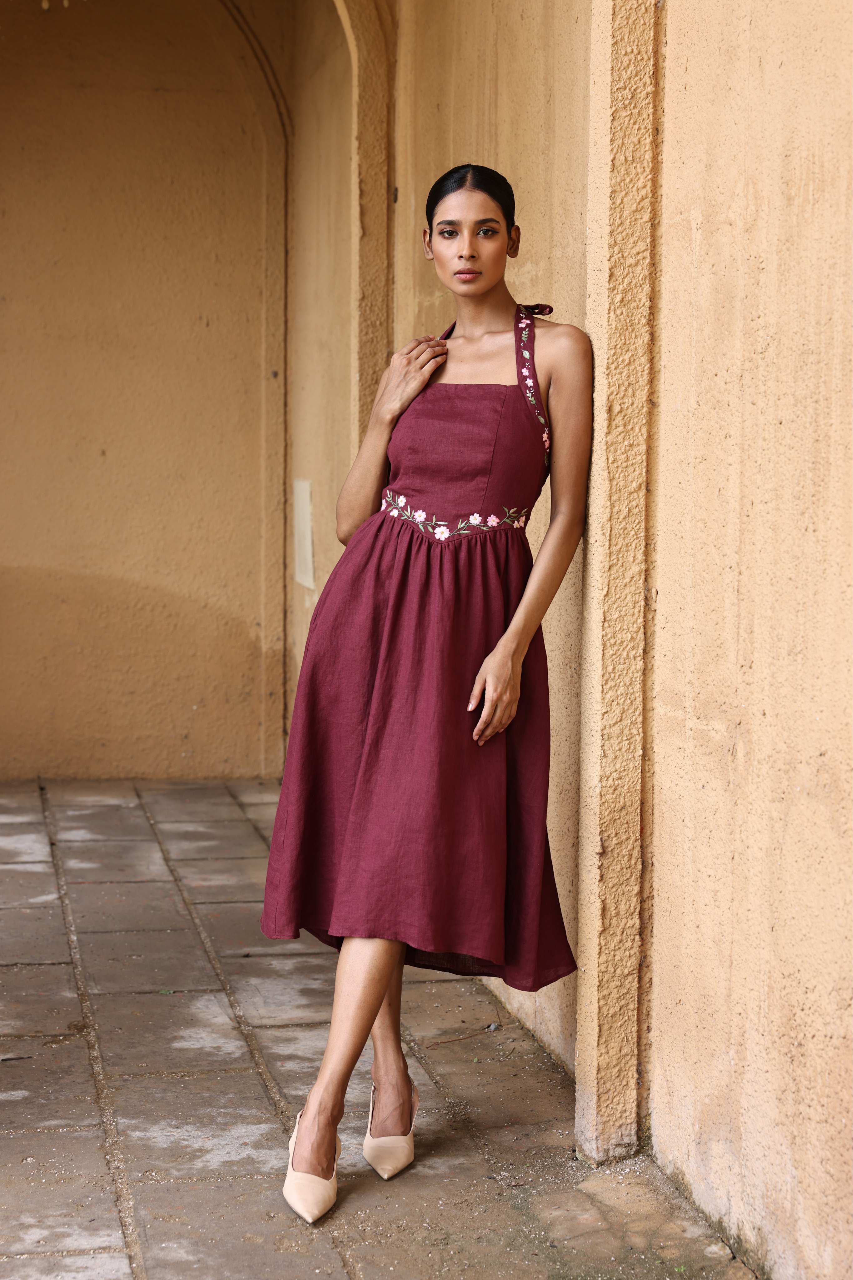 Woman in a burgundy dress standing against a beige wall.