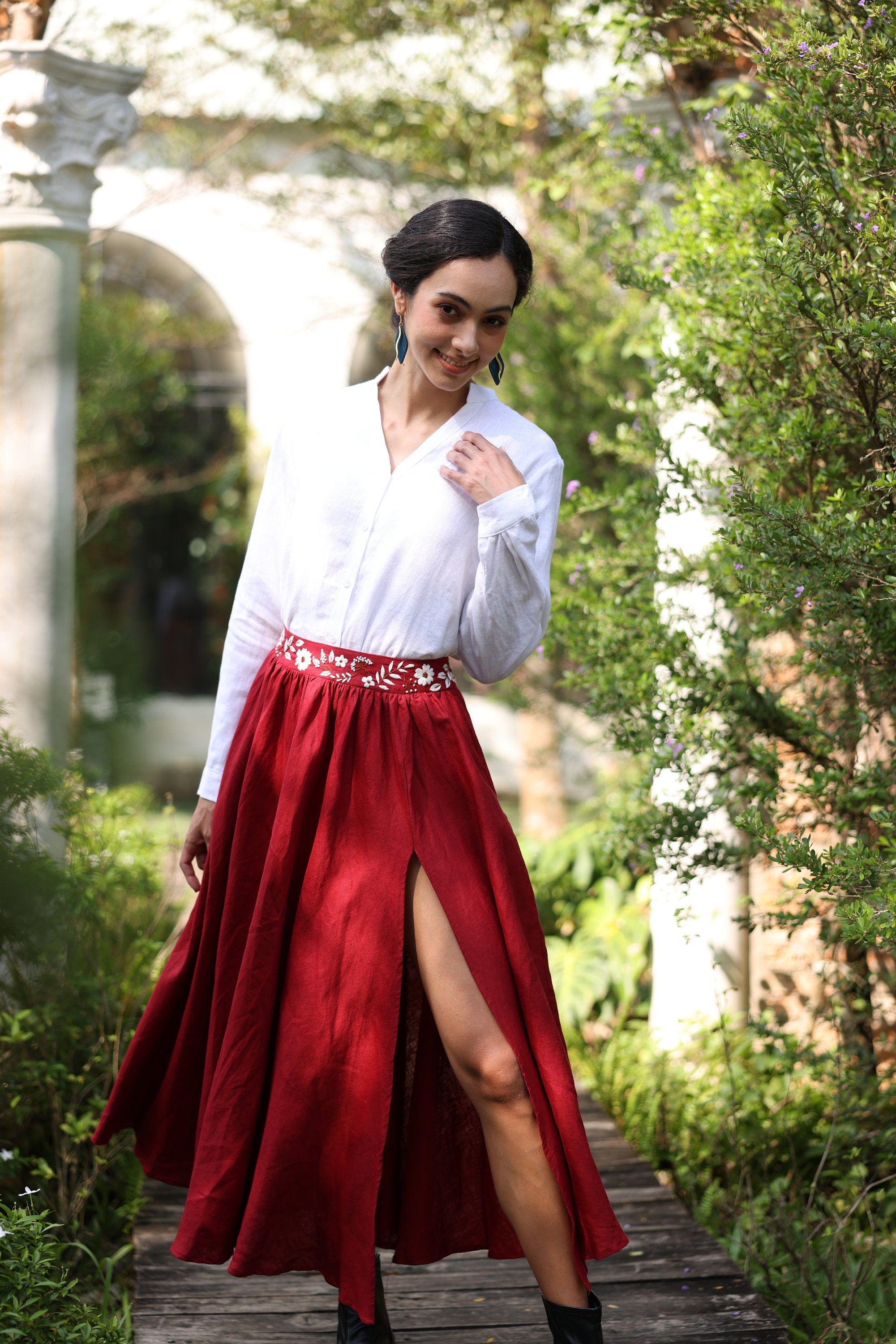 Woman in a white blouse and red skirt standing in a garden setting