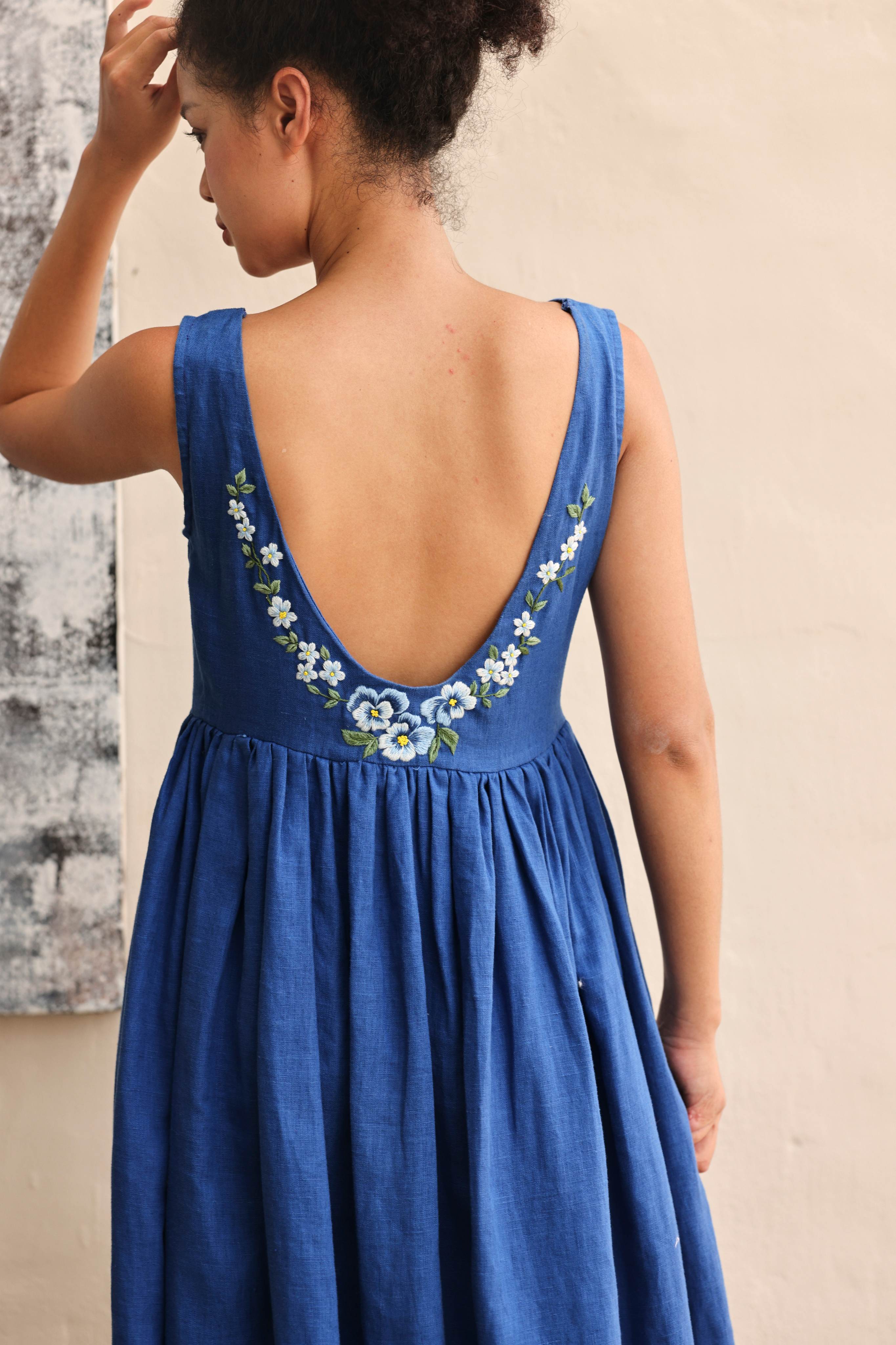 Woman wearing a blue dress with floral design against a beige wall.