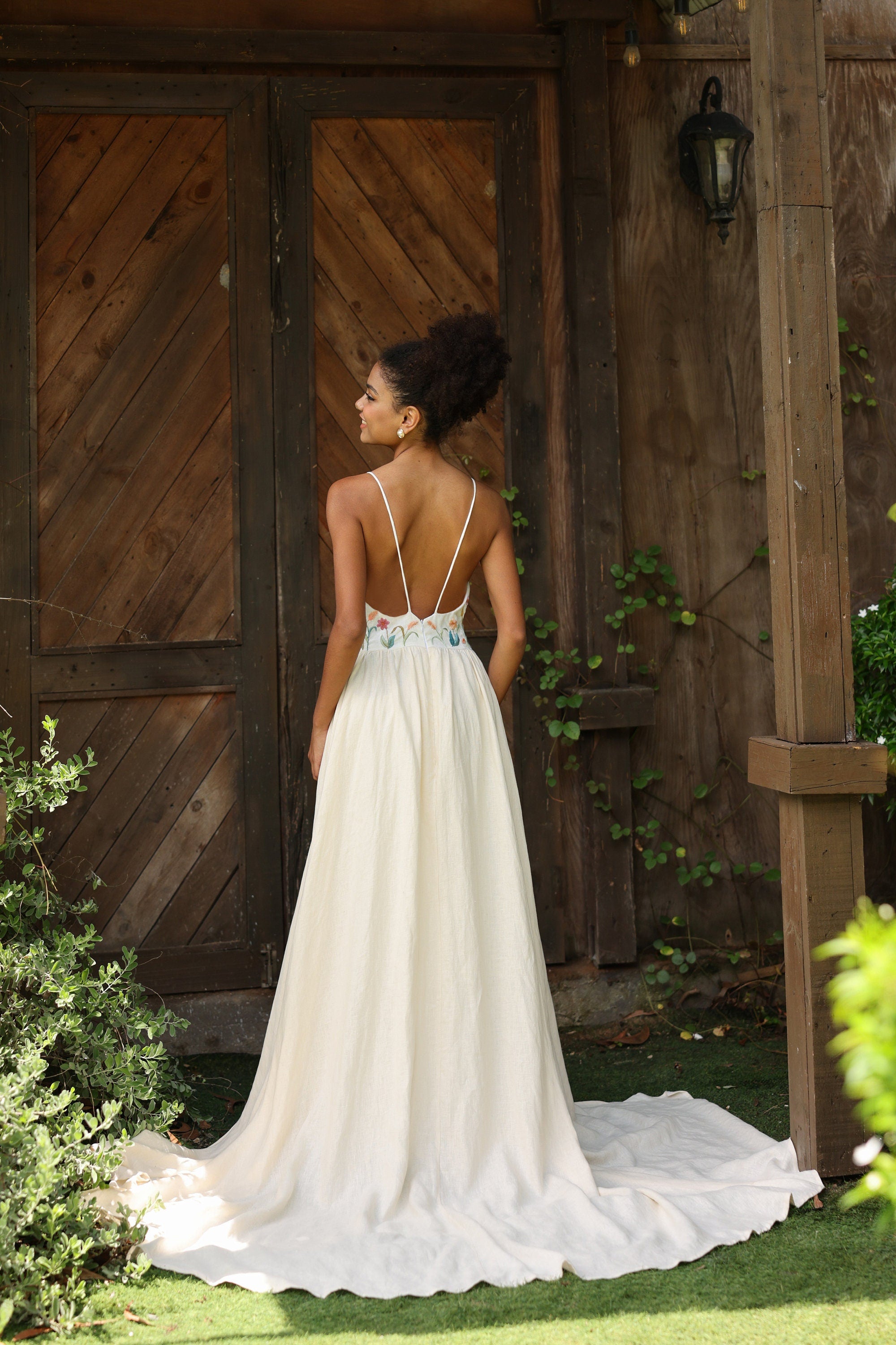 Woman in an ivory wedding dress with a backless design standing in front of a wooden door.
