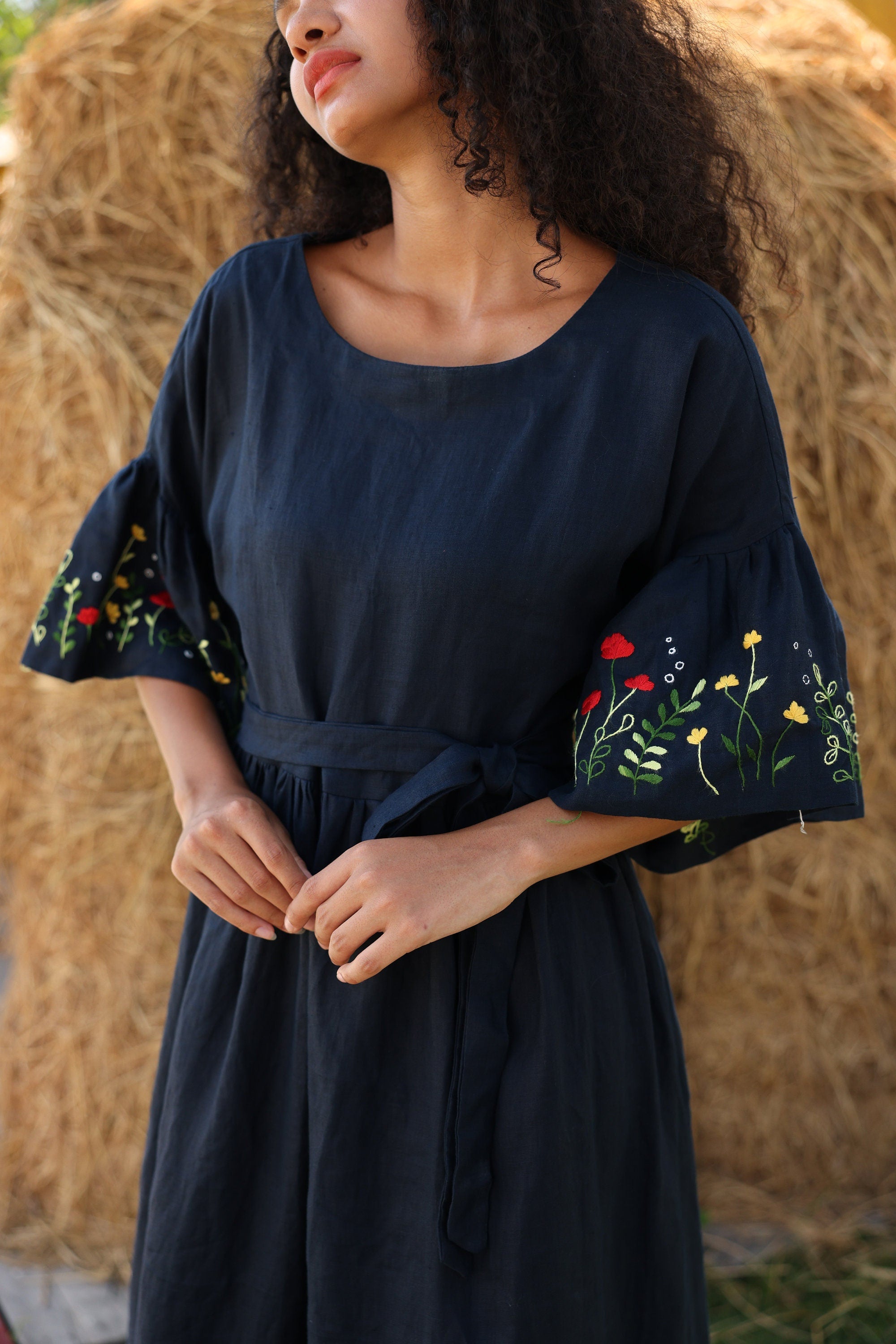 Woman wearing a navy blue dress with floral embroidery on sleeves against a rustic background
