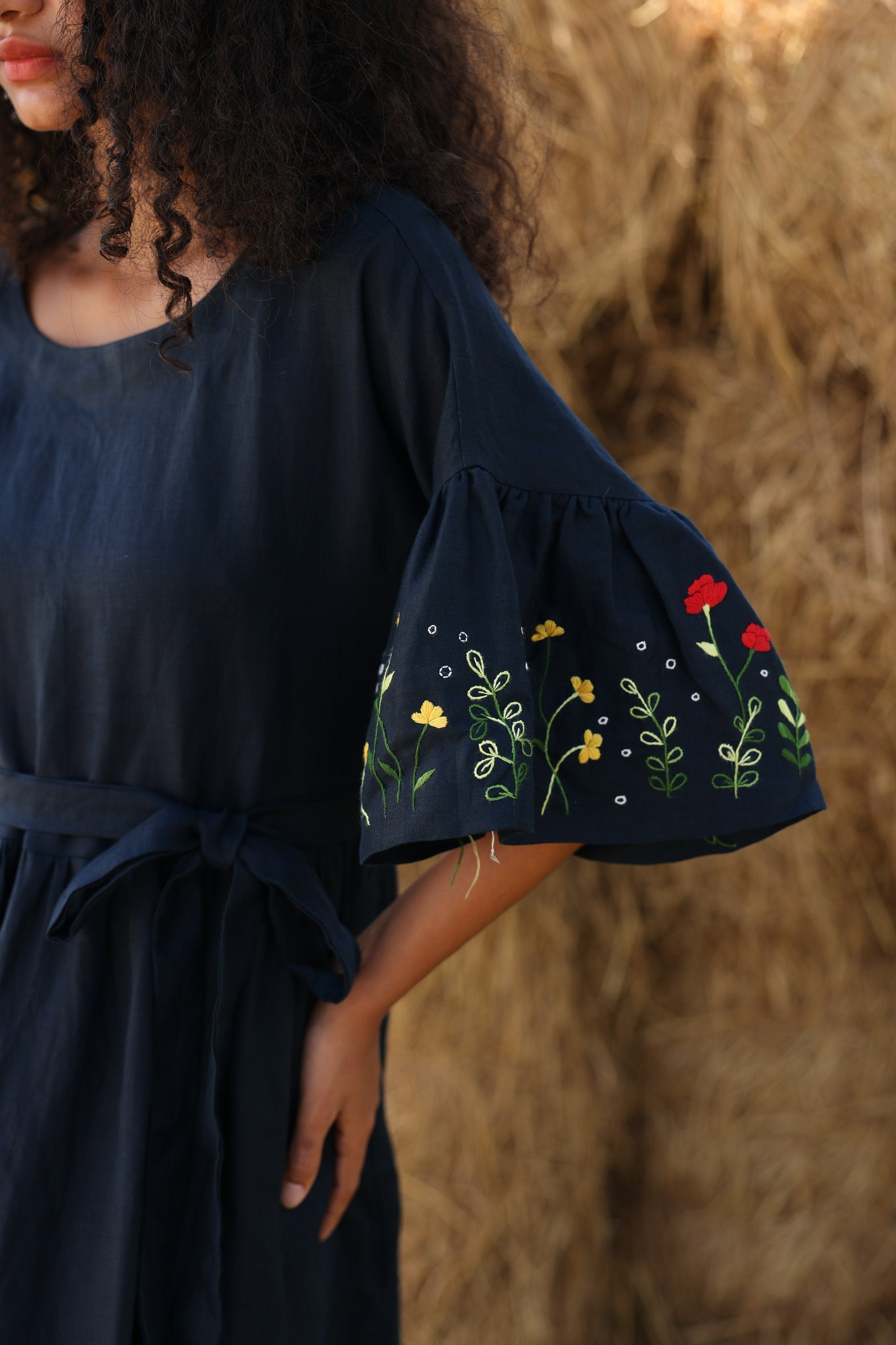 Navy blue dress with floral embroidery on sleeves against a blurred natural background