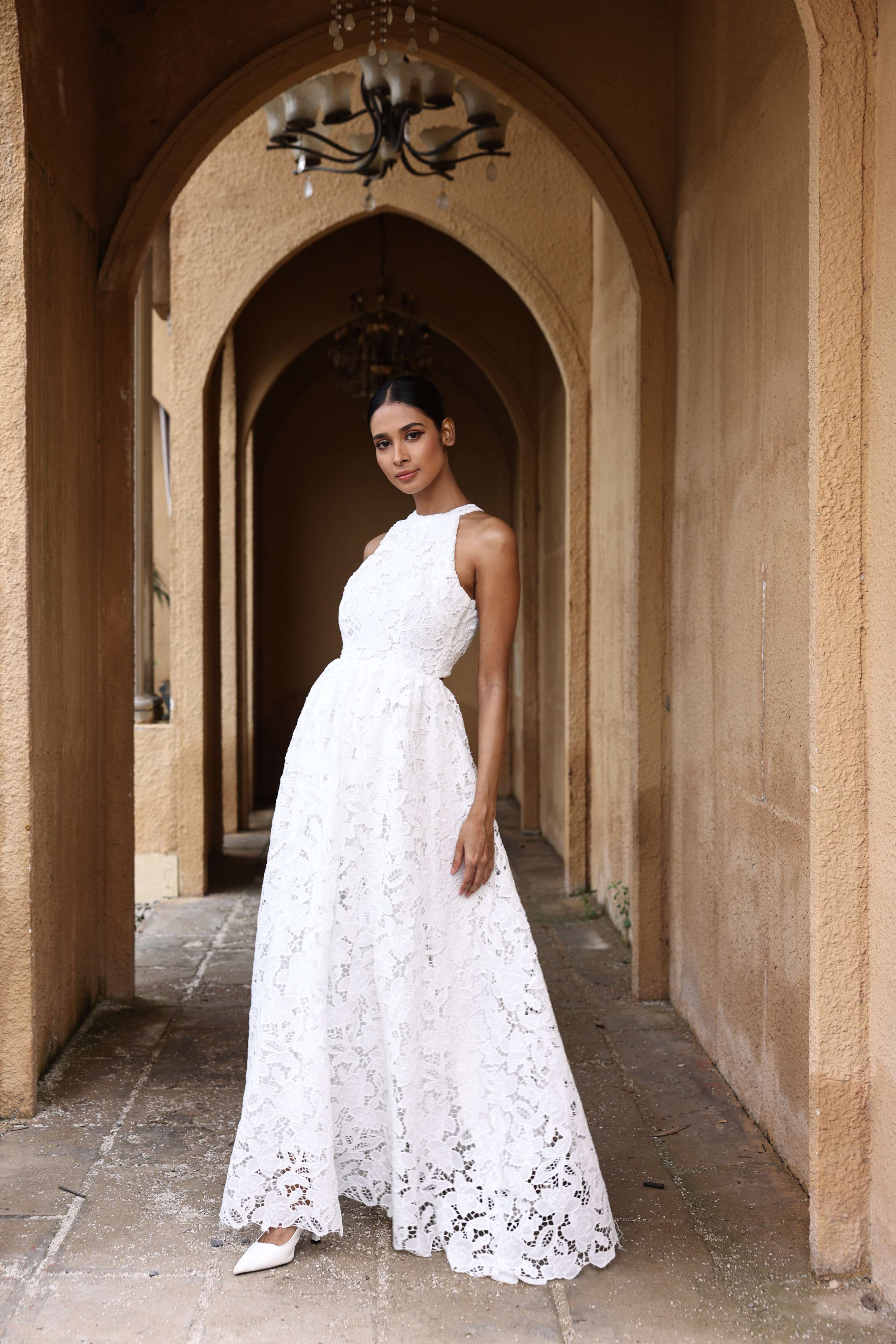 Woman in a white lace dress standing in an arched corridor.