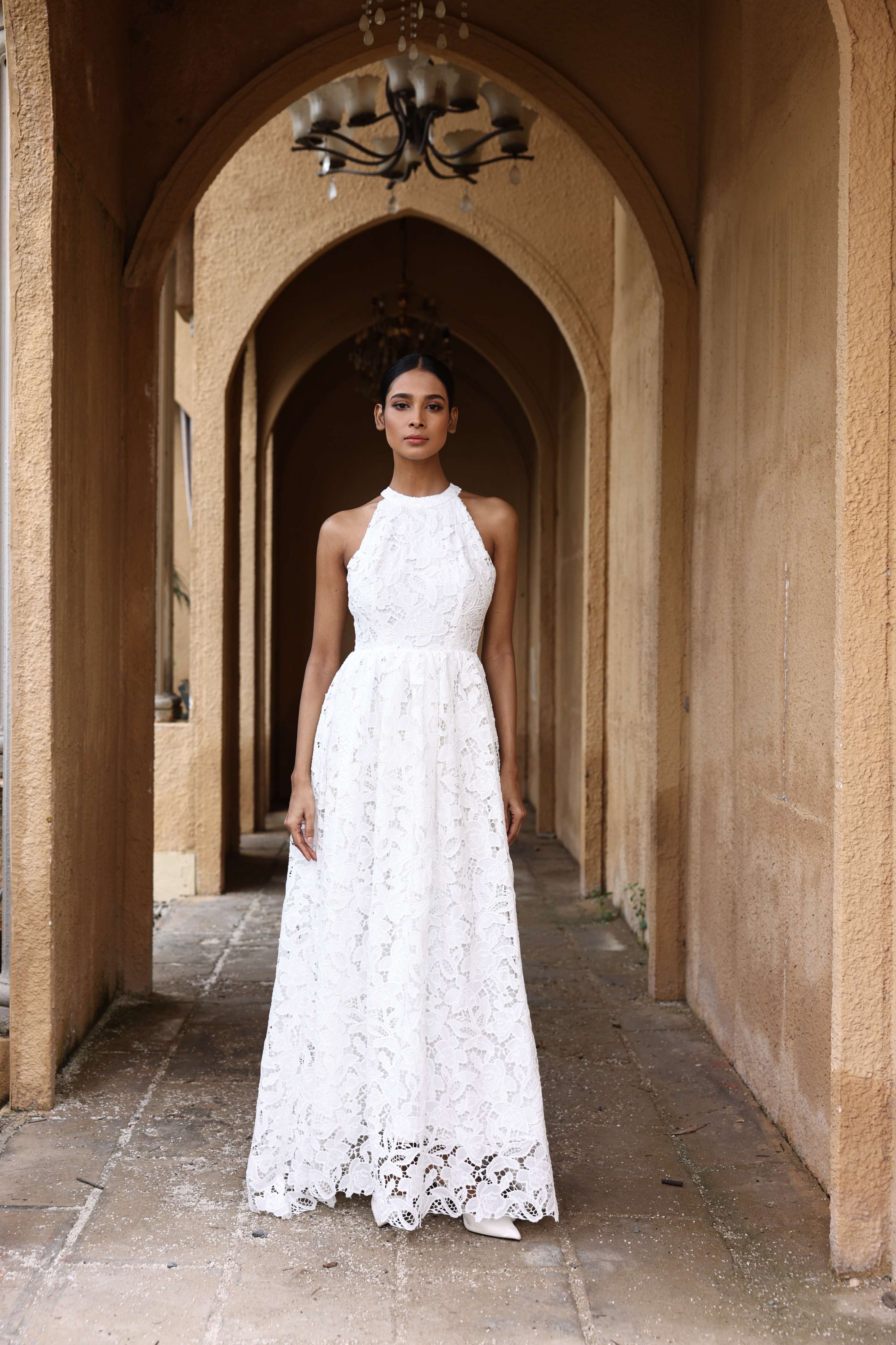 Woman in a white lace dress standing in an arched stone corridor.