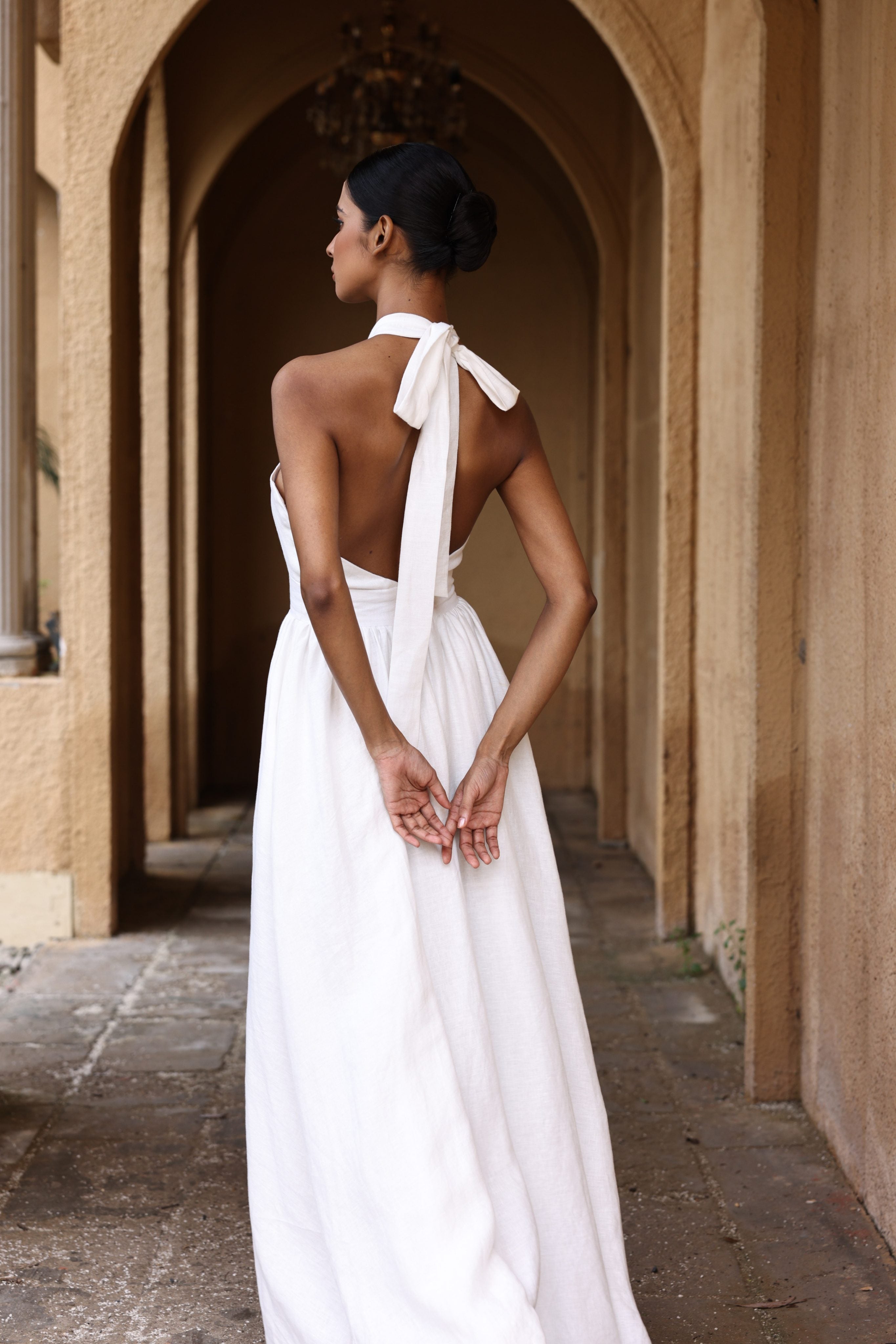 Woman in a white dress with a bow at the back standing in an arched stone corridor.