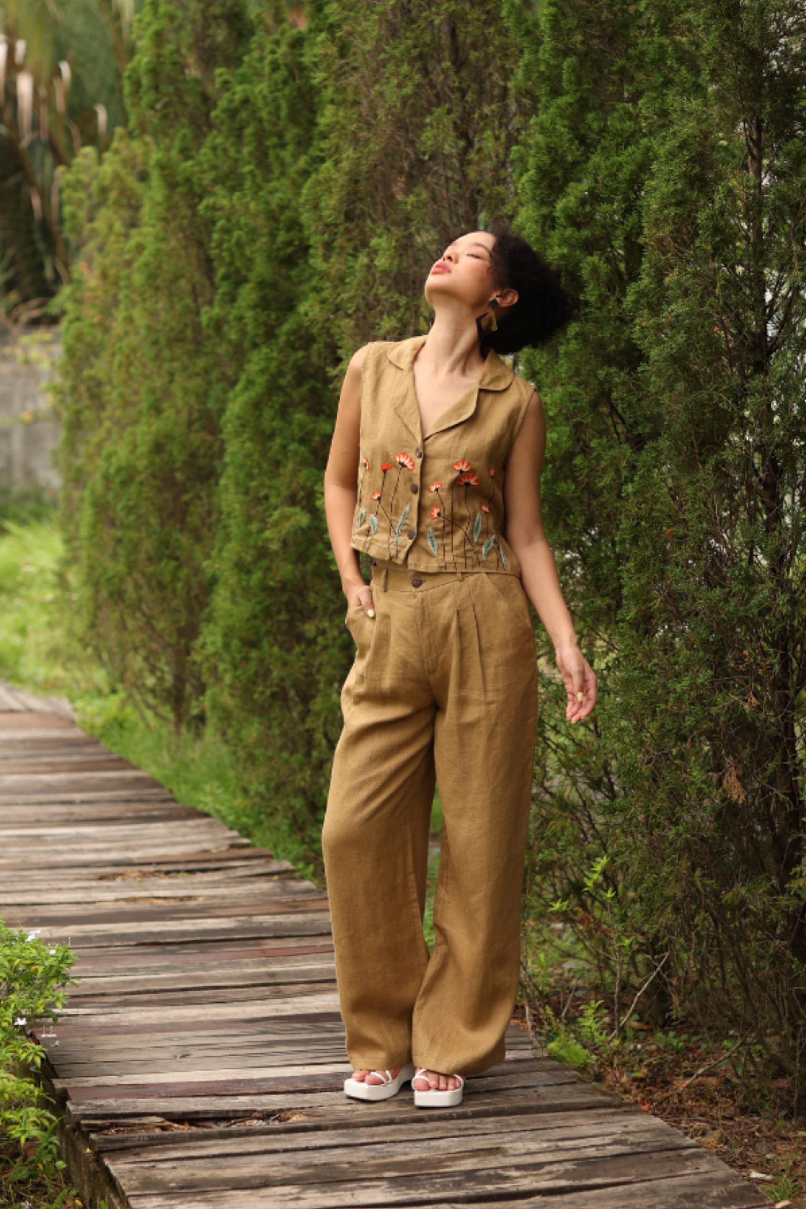 Woman in a beige outfit standing on a wooden path with greenery around