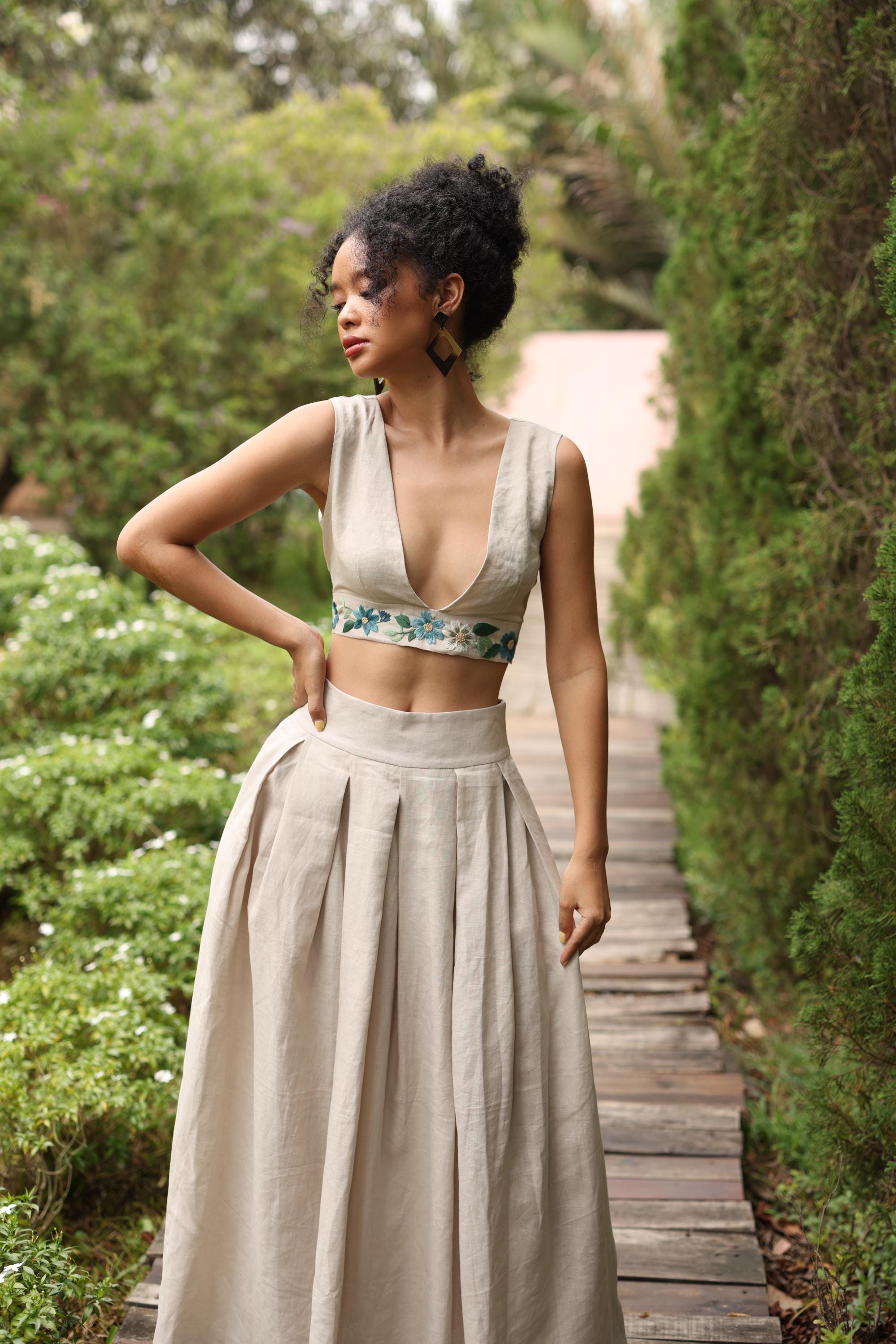 Woman in a beige sleeveless top and skirt standing in a garden path.