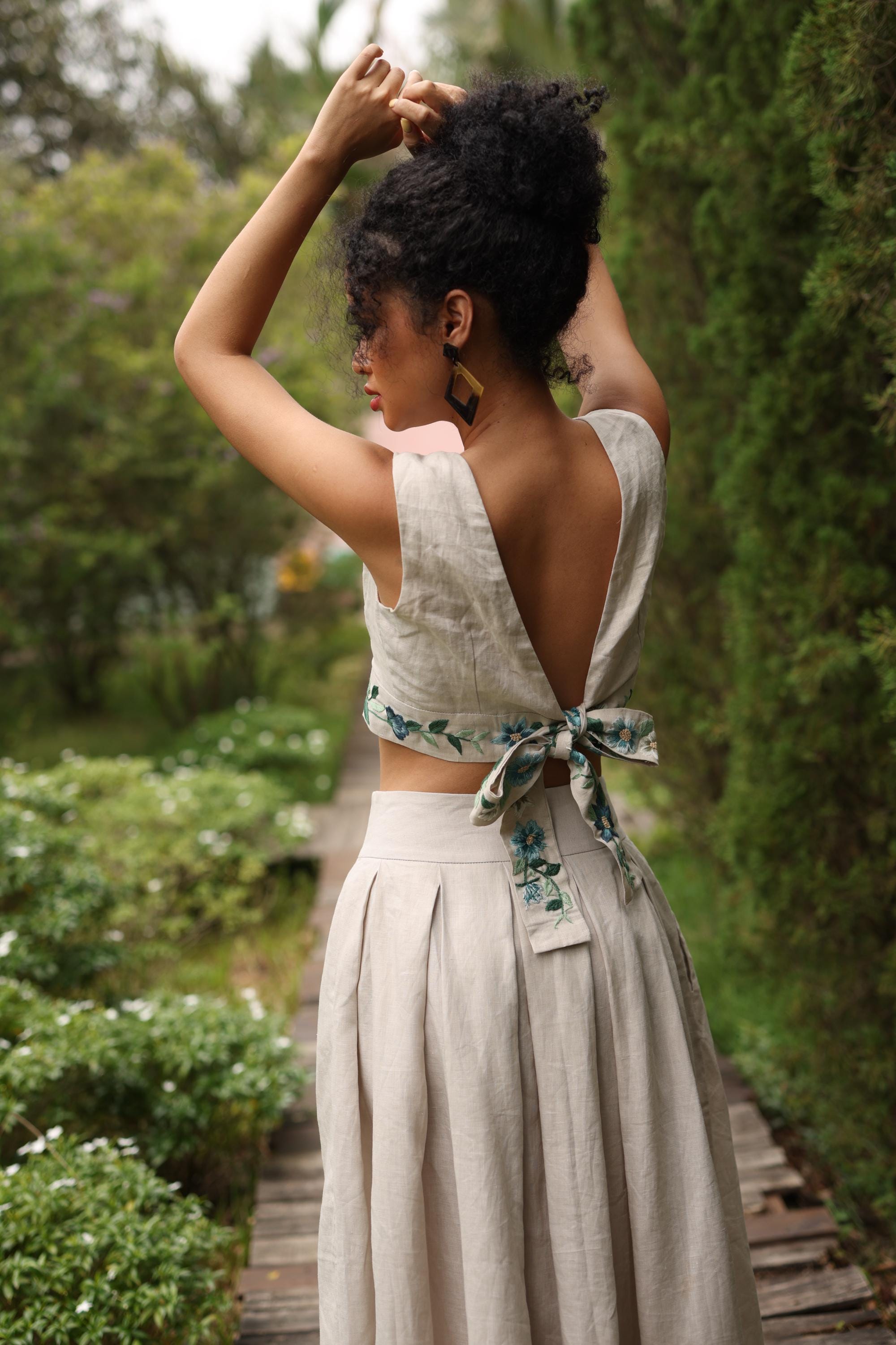 Woman in a light-colored top with floral details standing in a garden.