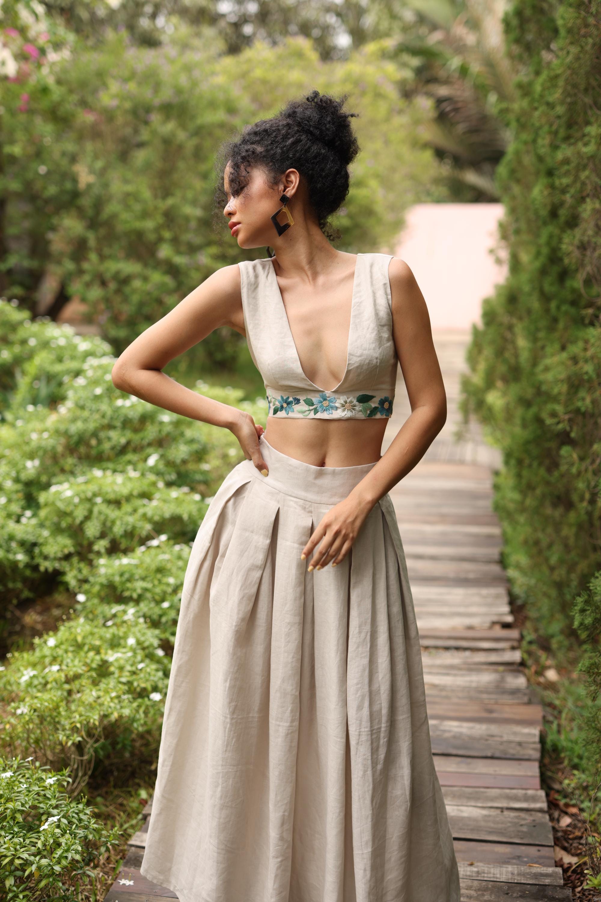 Woman in a flowing skirt standing on a wooden path surrounded by greenery