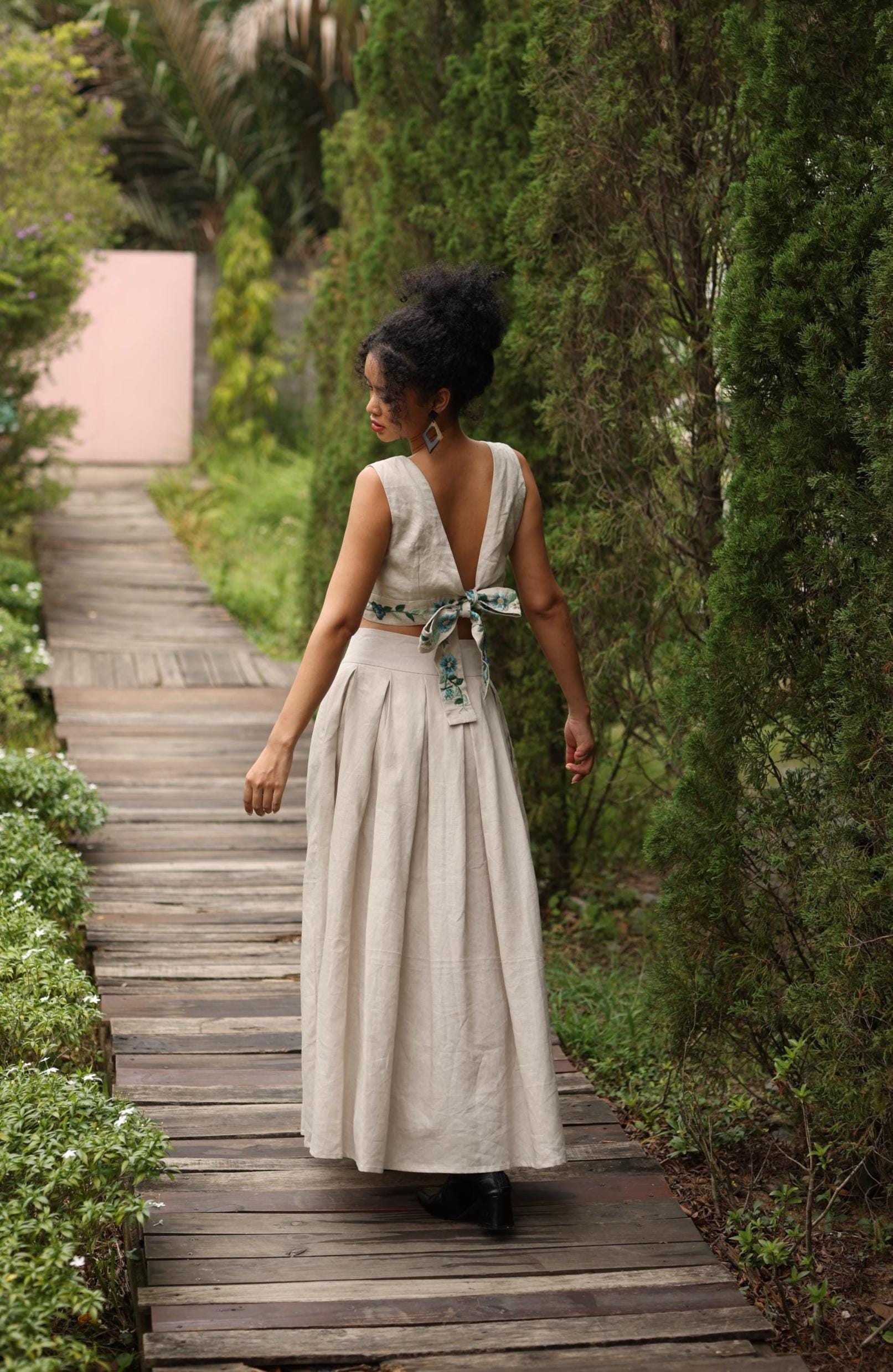 Woman in a flowing skirt walking on a wooden path in a garden