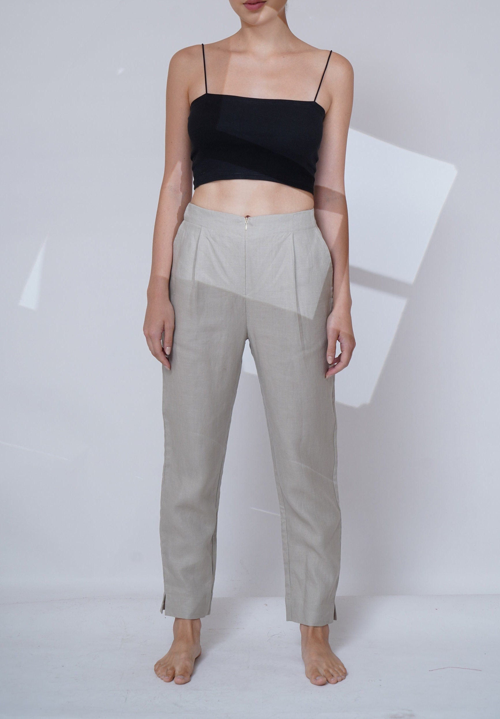 Person wearing a black top and light gray pants on a white background