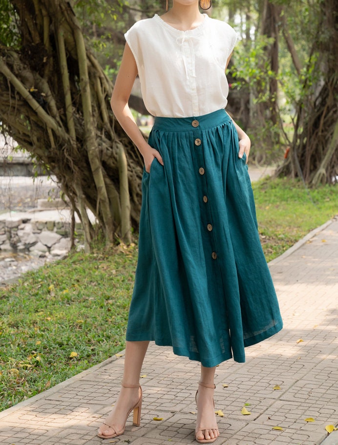 Woman wearing a white blouse and teal skirt with buttons outdoors.