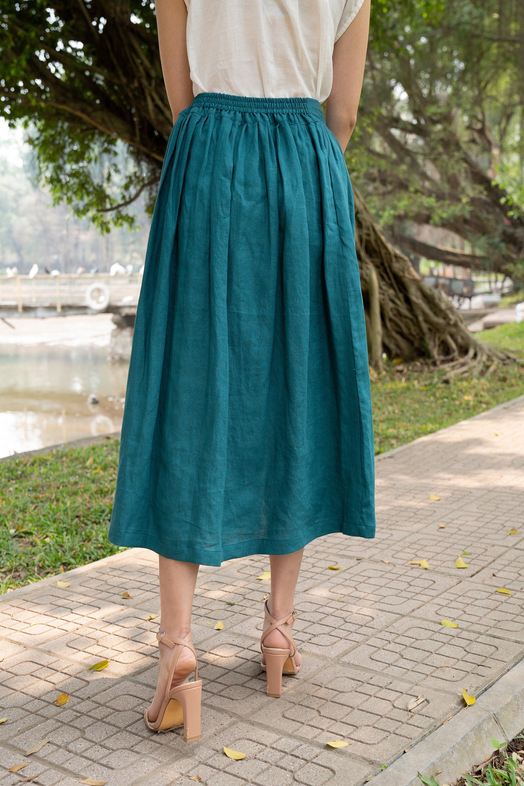 Person wearing a teal skirt standing on a sidewalk with greenery in the background