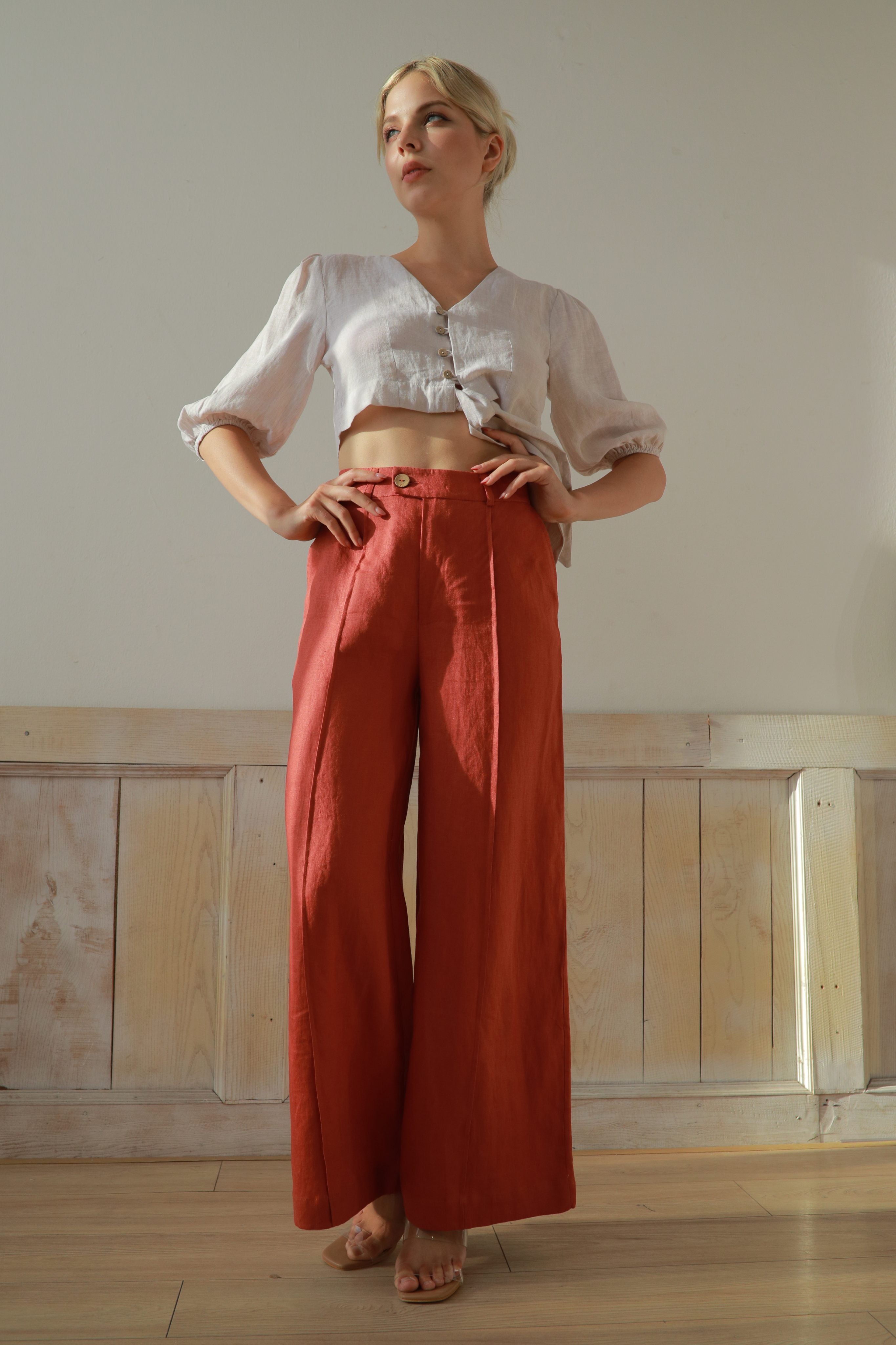 Woman wearing a white blouse and red pants standing in a room with wooden paneling.