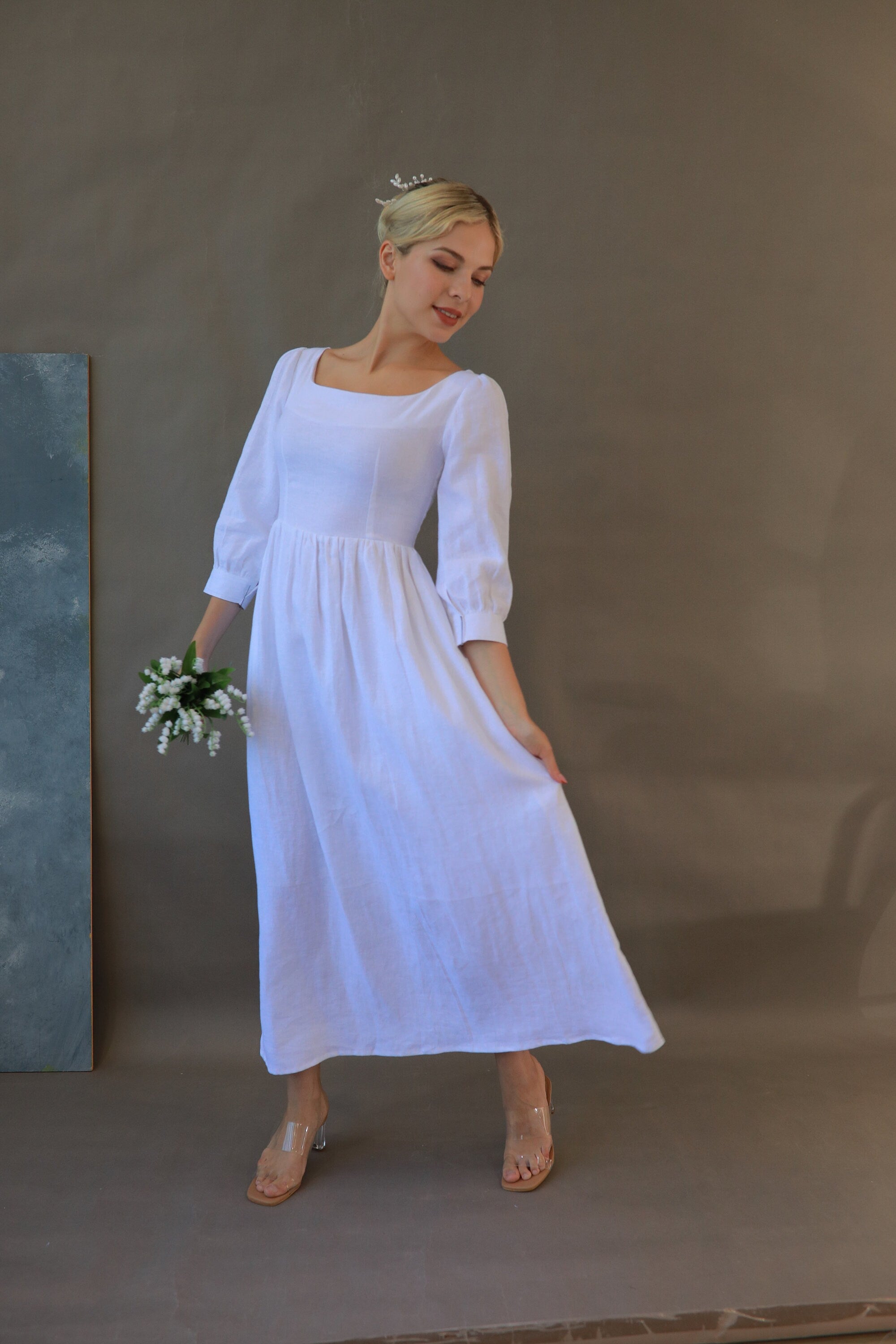 Woman in a white dress holding flowers against a plain background