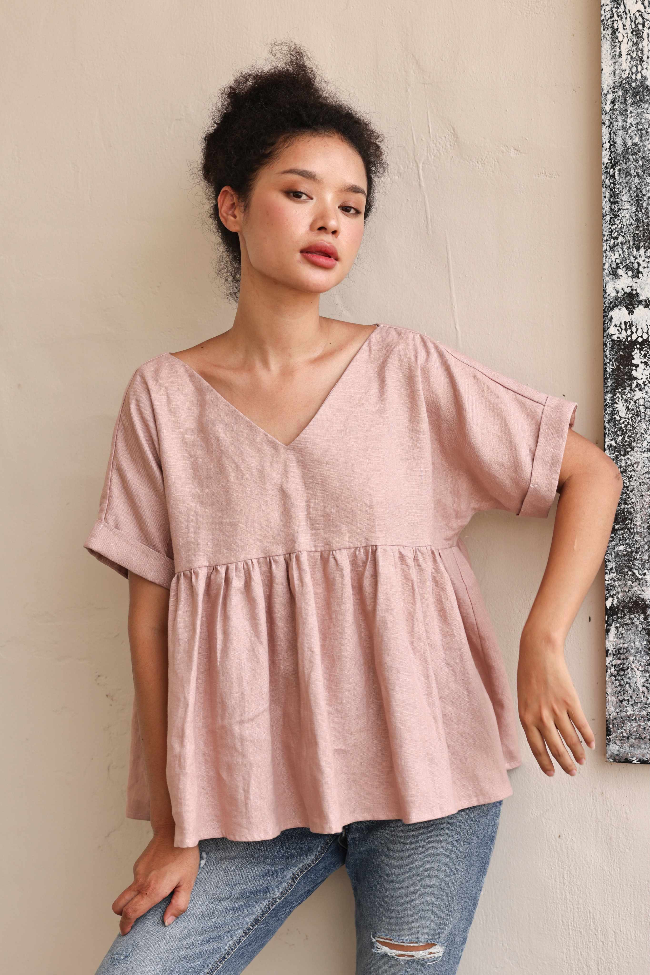 Woman wearing a pink blouse and jeans against a neutral wall.