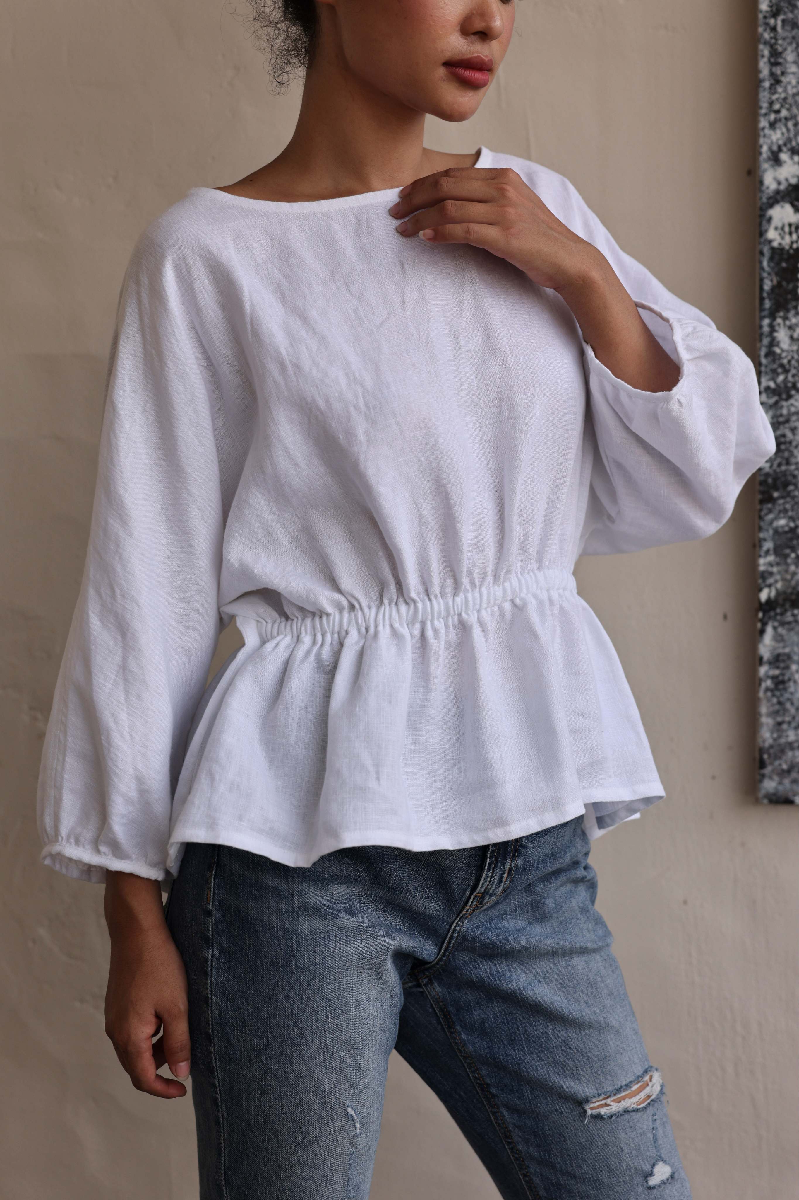 Person wearing a white blouse and blue jeans against a neutral background