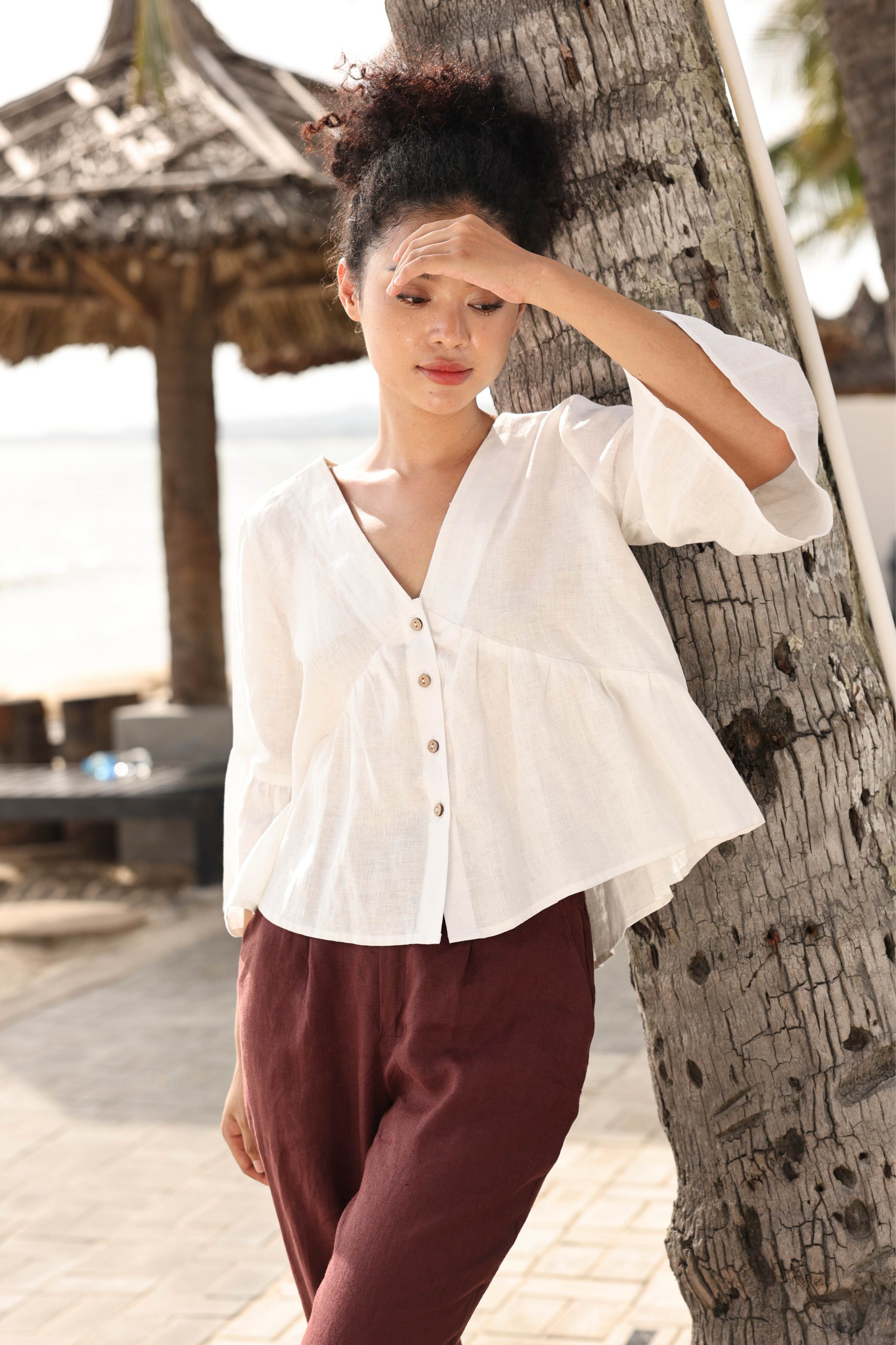 Woman in a white blouse and maroon pants leaning against a tree