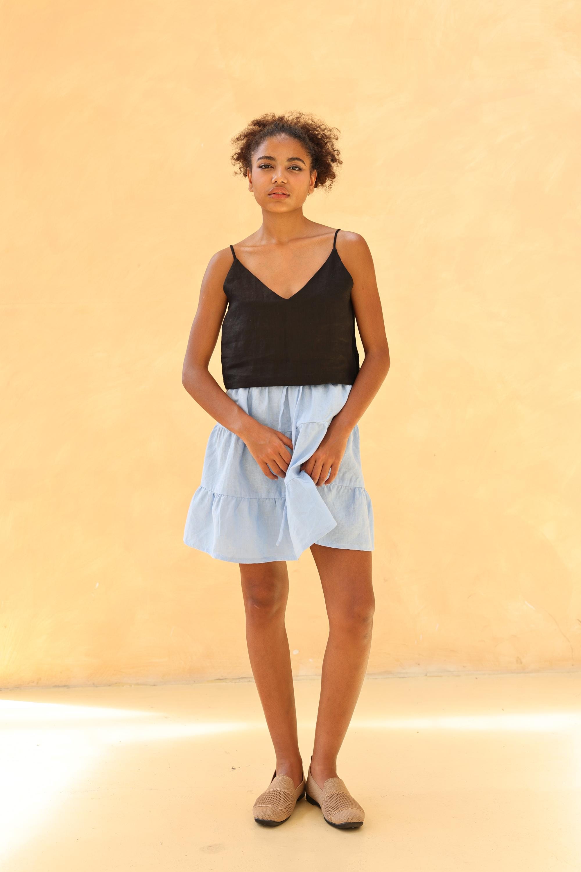 Woman wearing a black tank top and light blue skirt against a beige background