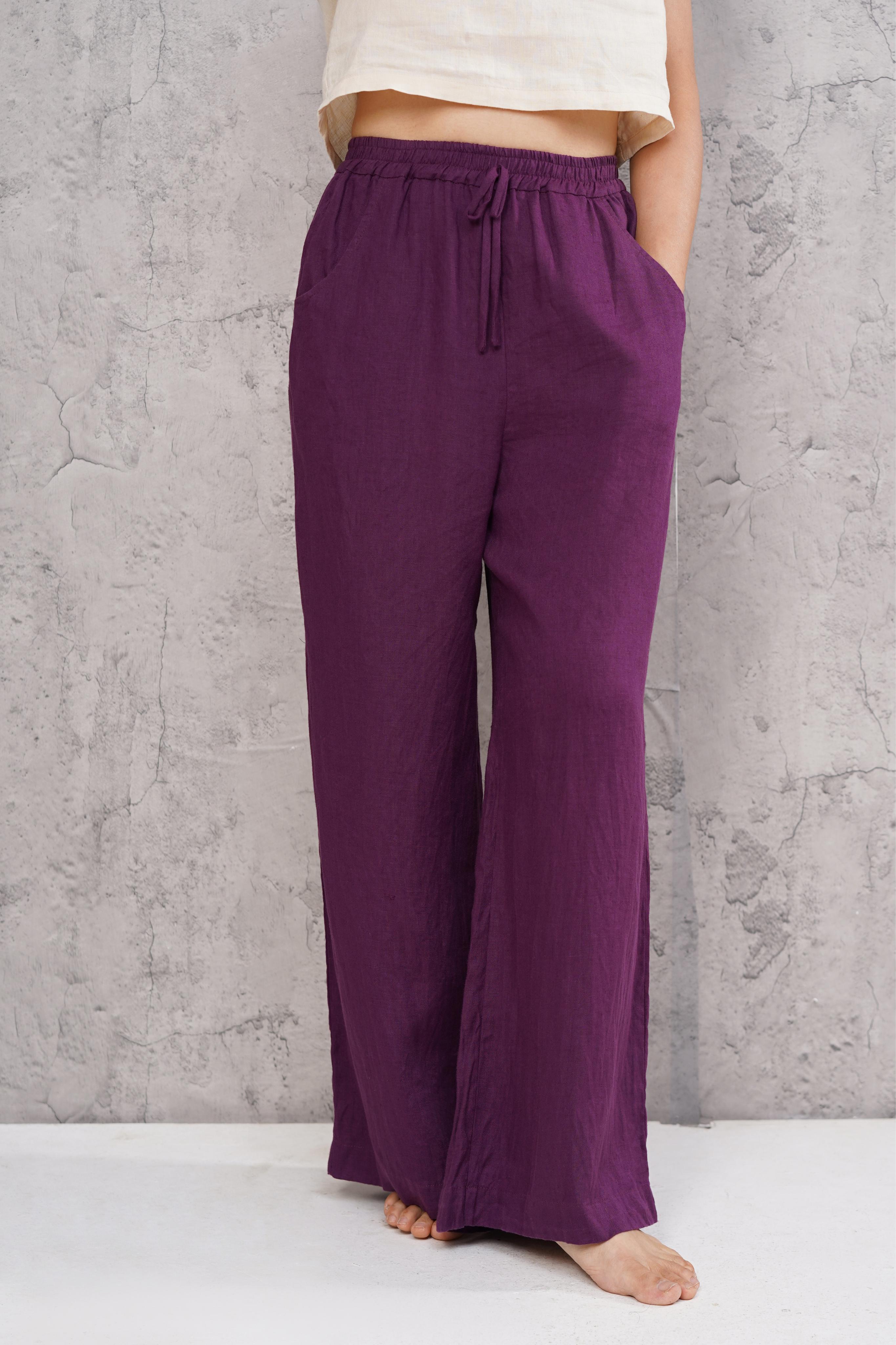 Purple wide-leg pants worn by a person against a gray concrete wall.
