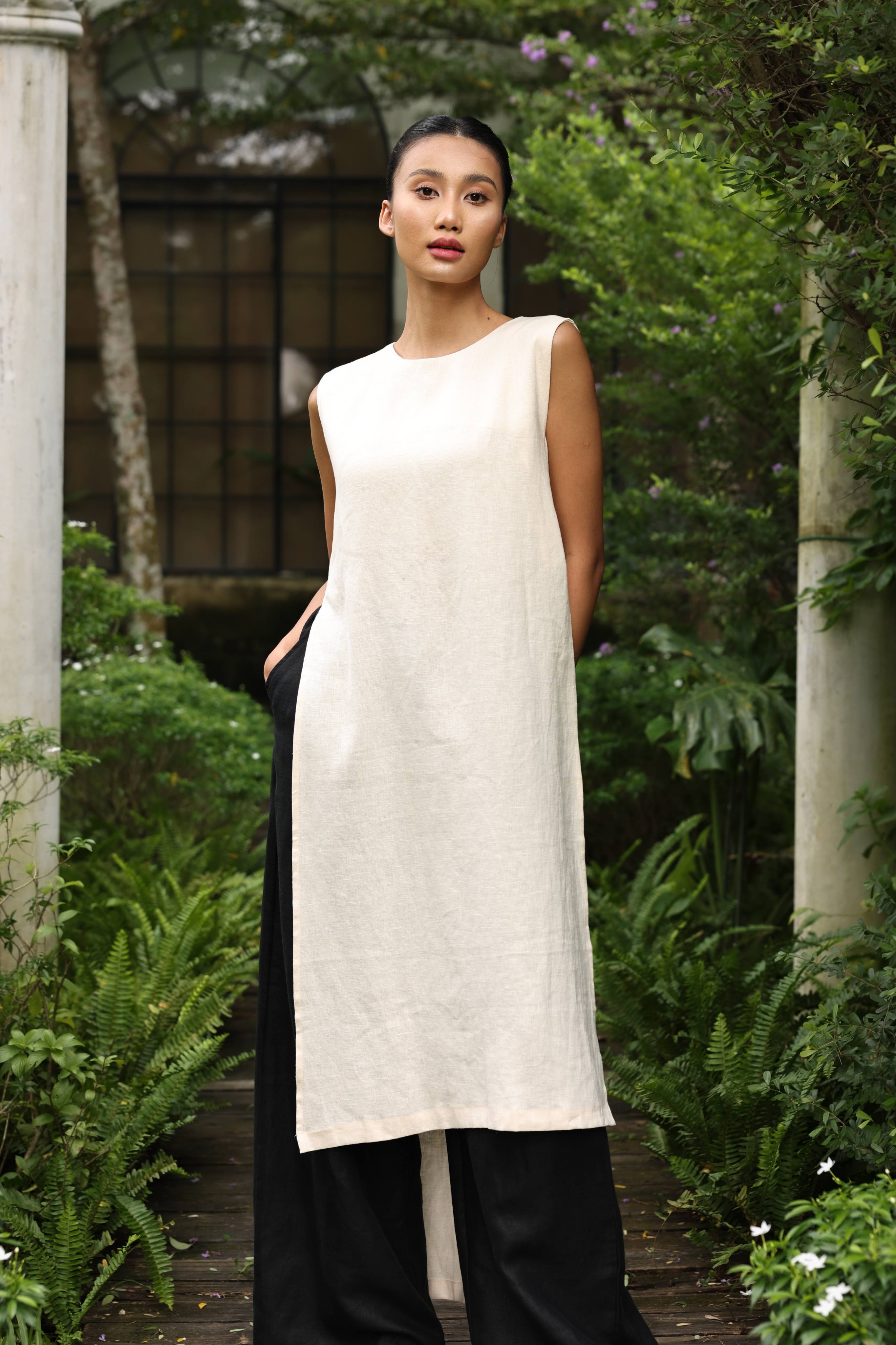 Woman wearing a white sleeveless dress with black pants in a garden setting