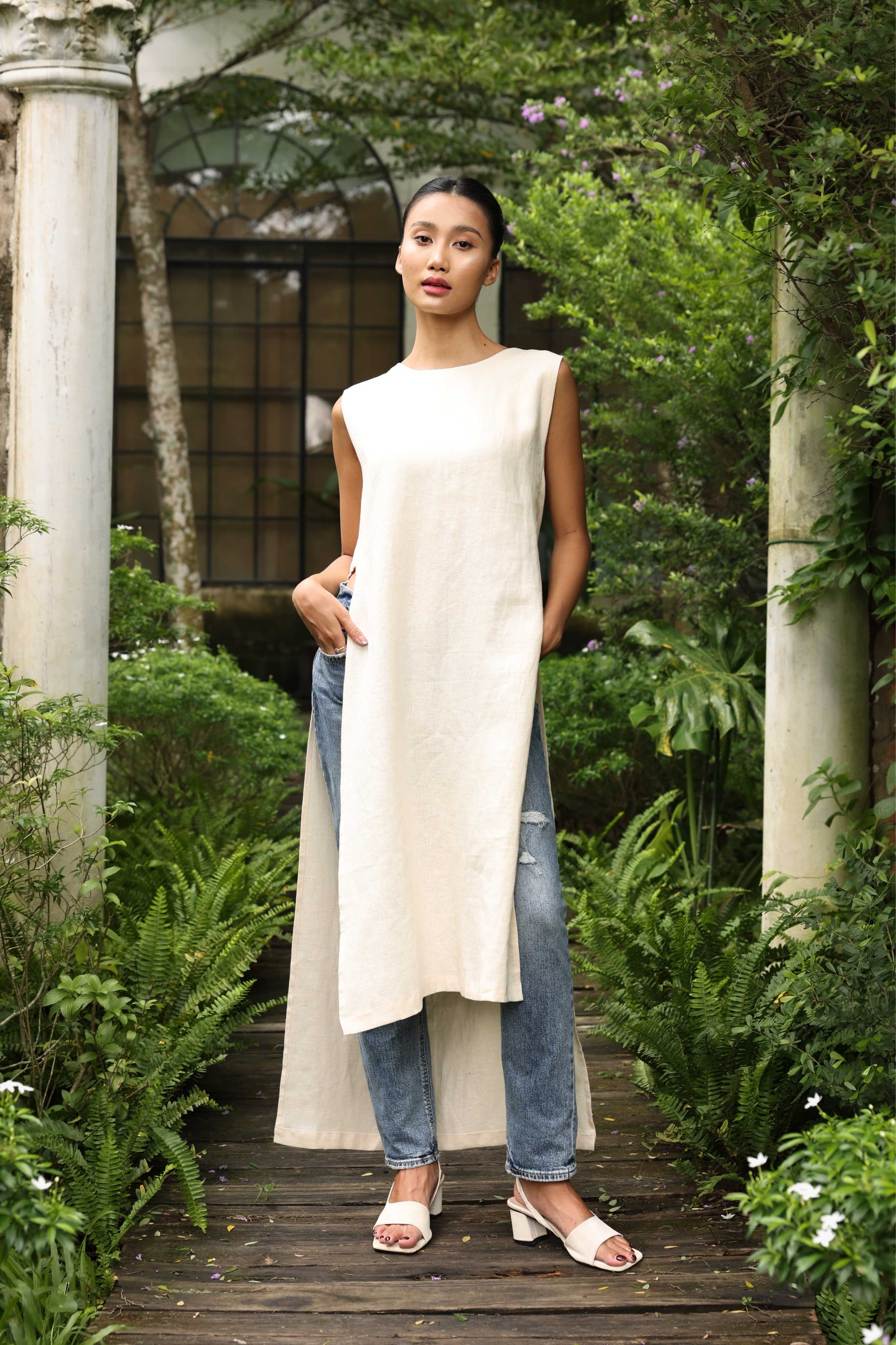 Woman wearing a long beige dress over jeans in a garden setting