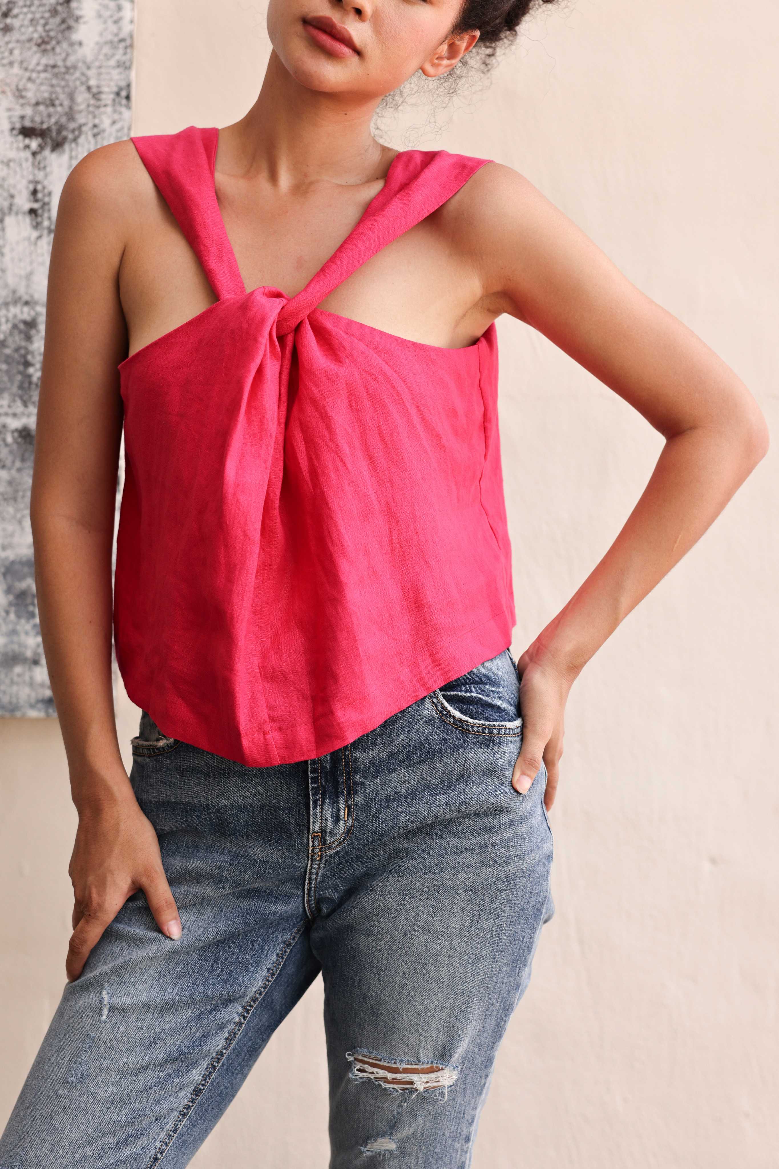Woman wearing a pink sleeveless top with a tie detail and blue jeans against a neutral background