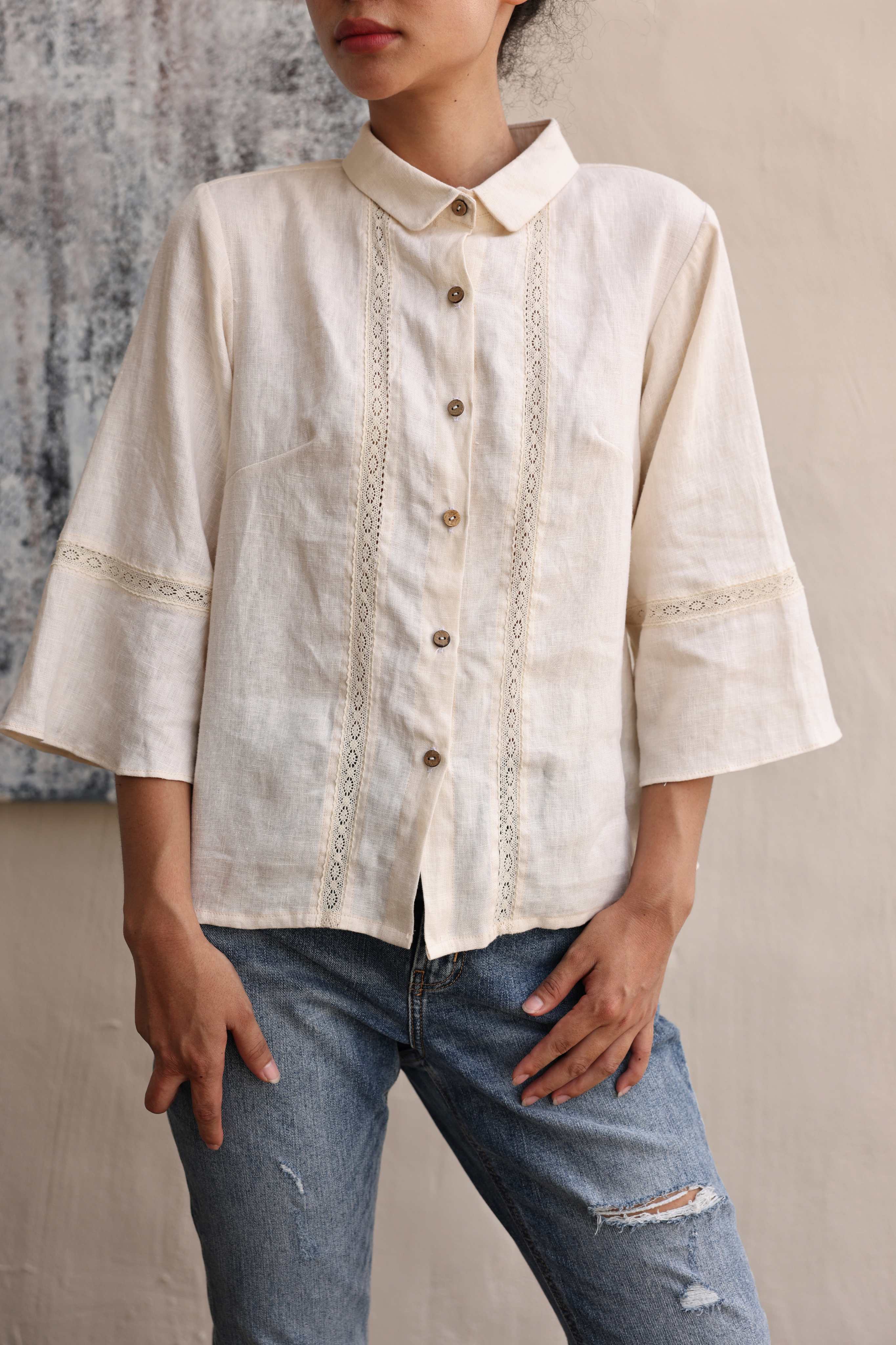 Person wearing a beige shirt and blue jeans against a neutral background